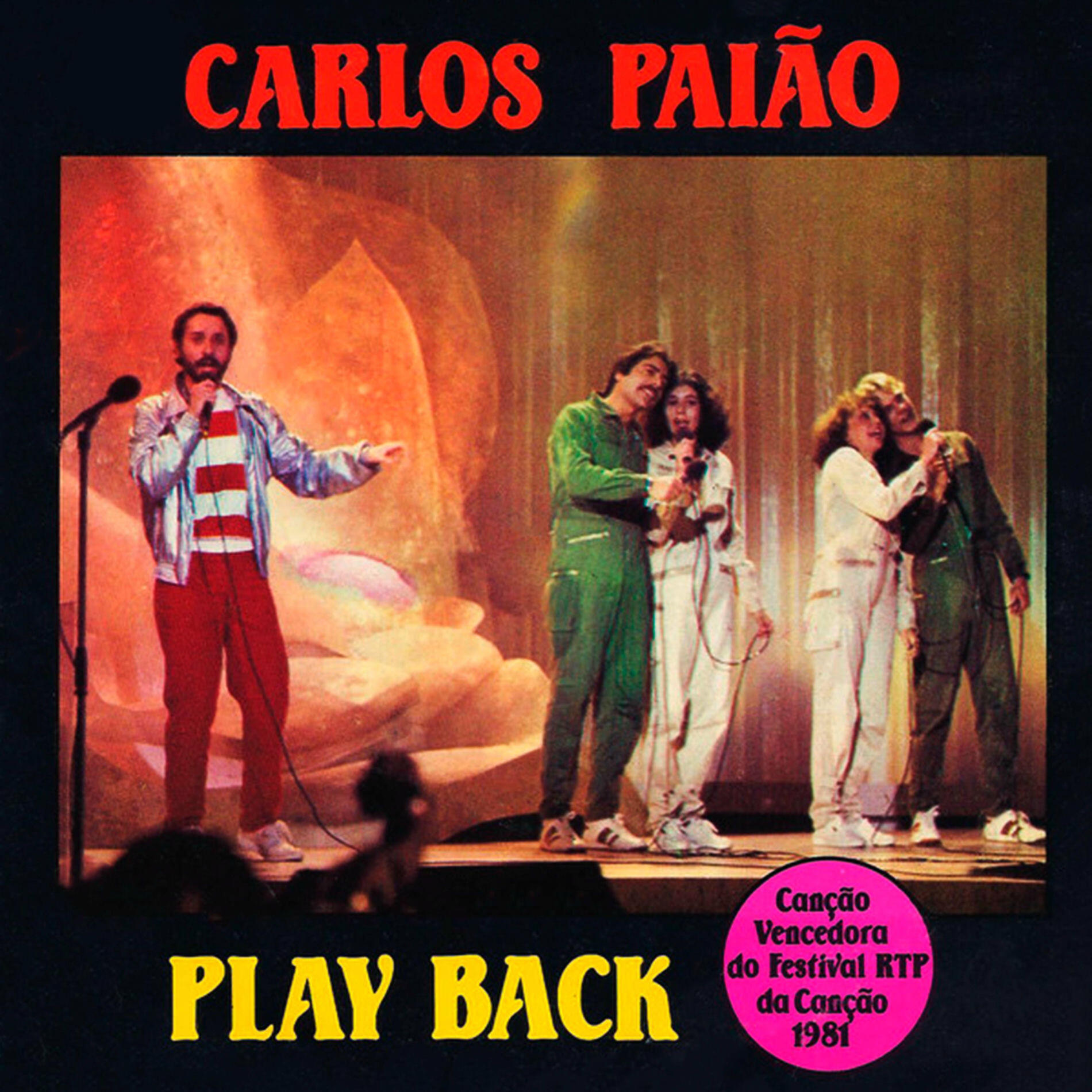 La portada de la canción «PlayBack» de Carlos Paião muestra a los artistas en el escenario, vestidos con trajes coloridos y micrófonos. Iluminación vibrante y texto superpuesto.