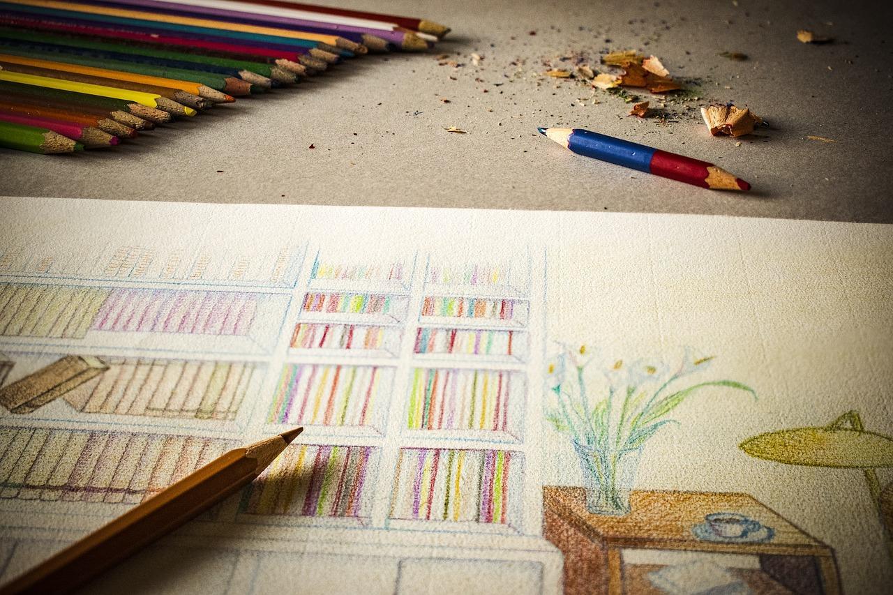 Lápices de colores sobre una mesa, junto a una hoja de papel con un plano de una casa.