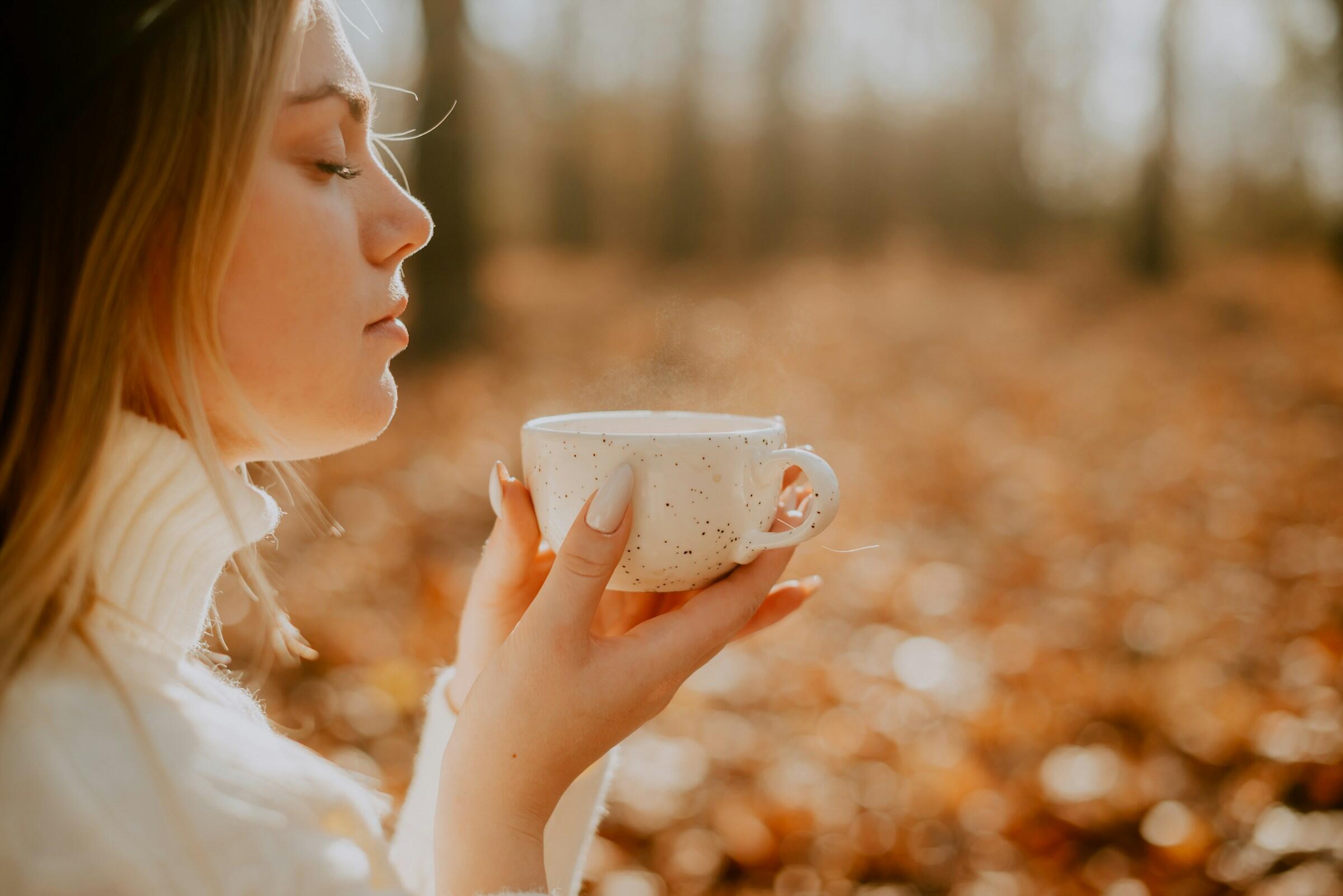 Persona sosteniendo una taza humeante en un bosque otoñal.