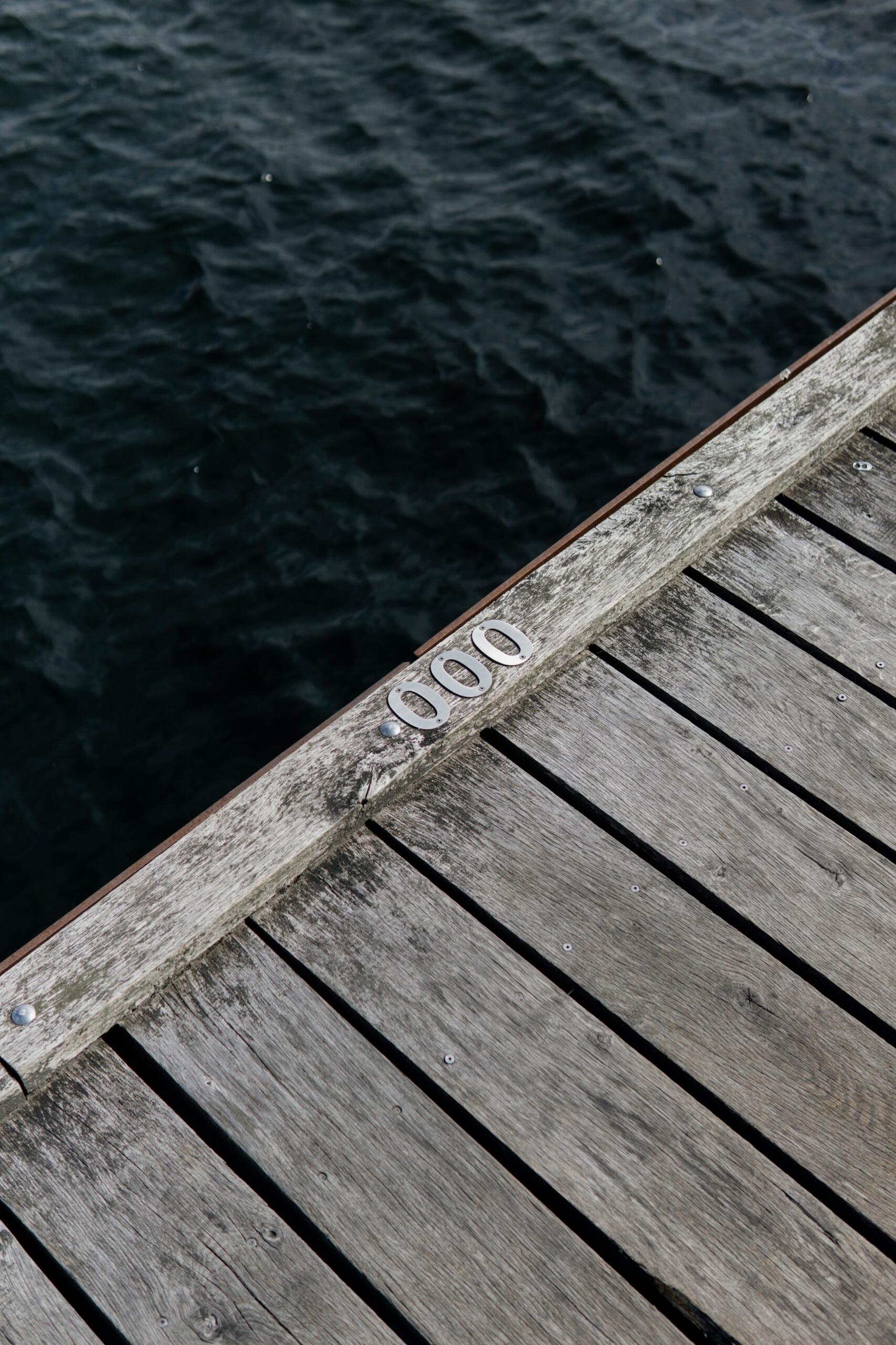 Borde de muelle de madera sobre agua oscura con lazos metálicos laterales.