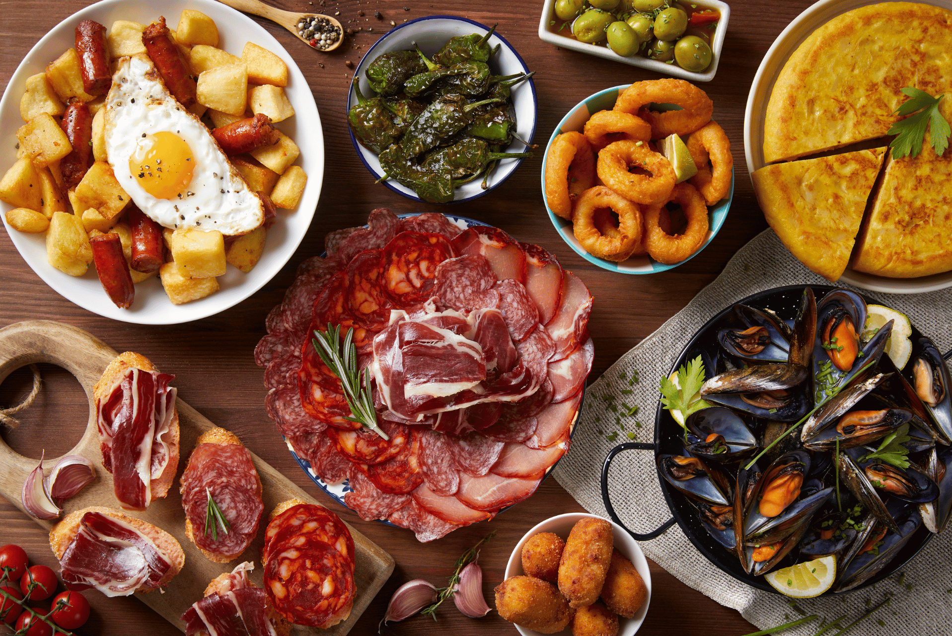 Surtido de tapas españolas que incluye carnes, mejillones, tortilla y calamares fritos.