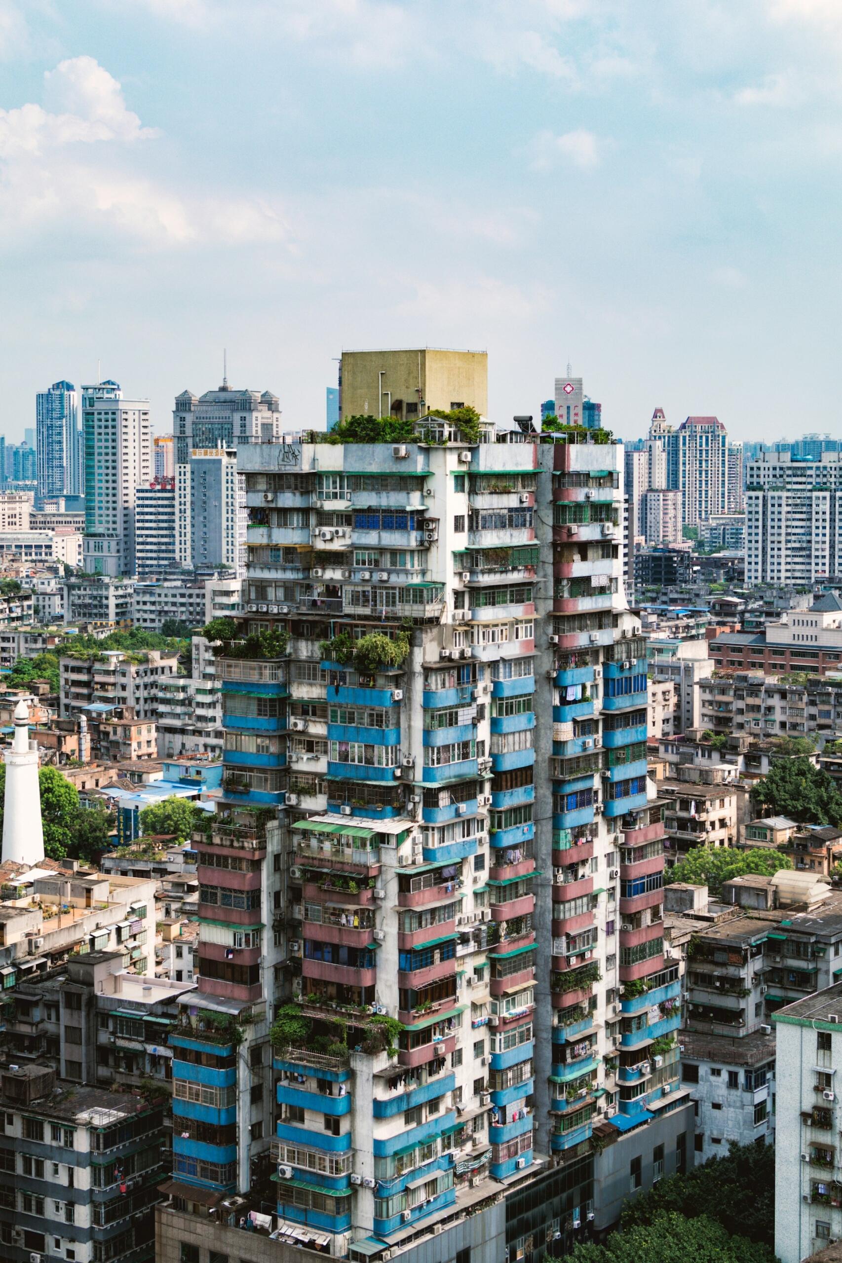 Un animado paisaje urbano en el que destaca un rascacielos de vivos colores con toques azules, verdes y rojos, rodeado de densas construcciones urbanas bajo un cielo parcialmente nublado.