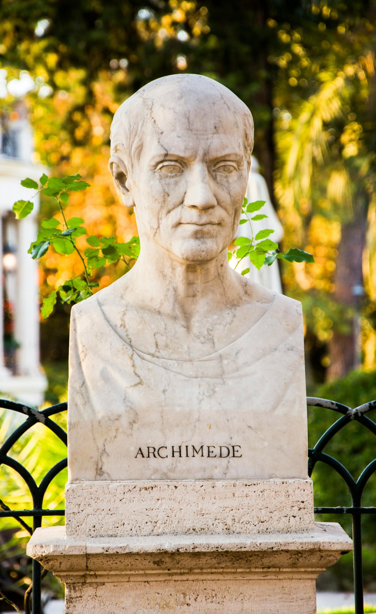 Busto de mármol sobre pedestal rotulado «ARCHIMEDE» con fondo verde natural.