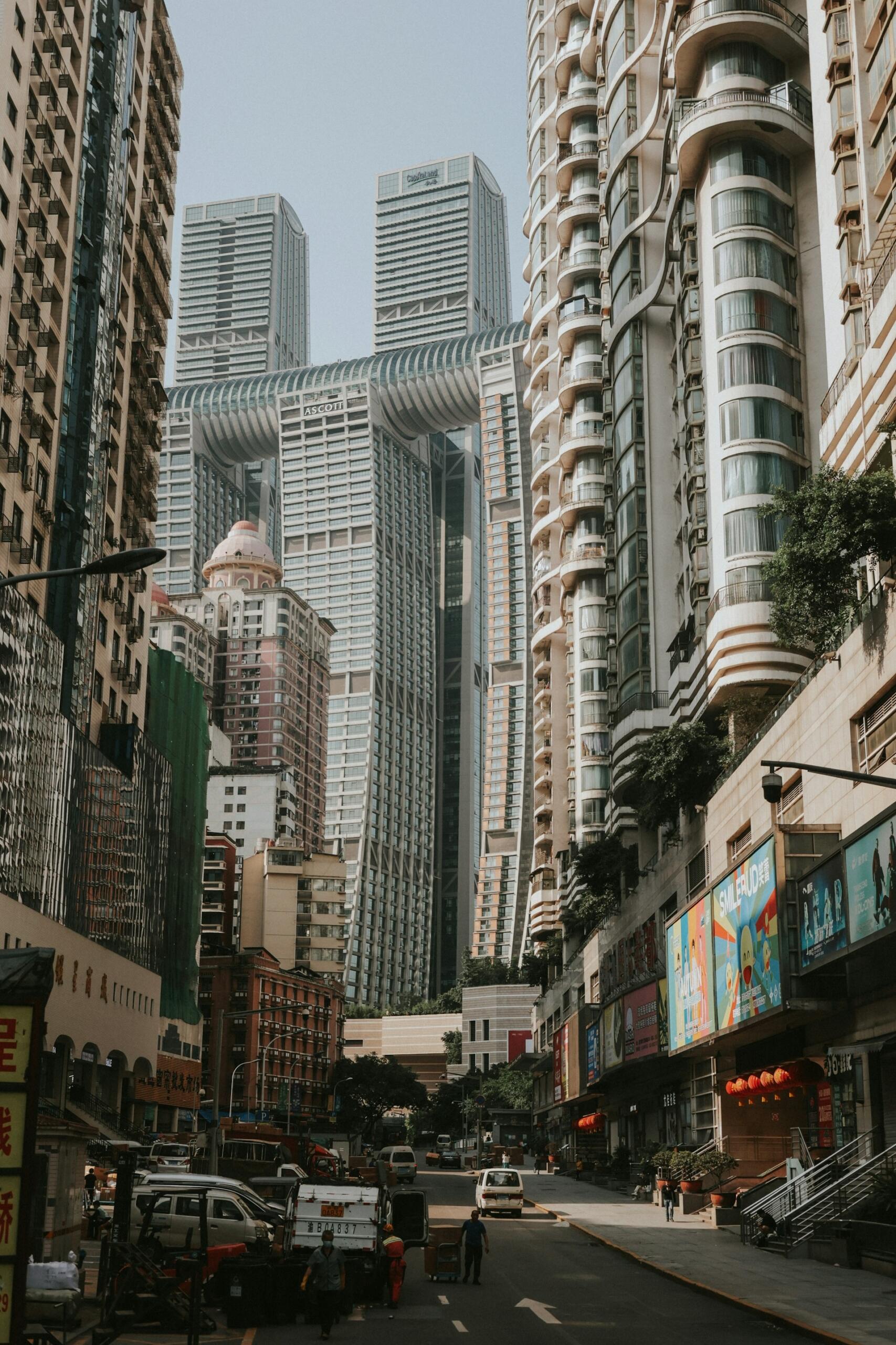 Una bulliciosa calle urbana flanqueada por altos rascacielos modernos y una mezcla de edificios más antiguos. La gente y los vehículos crean un ambiente animado.