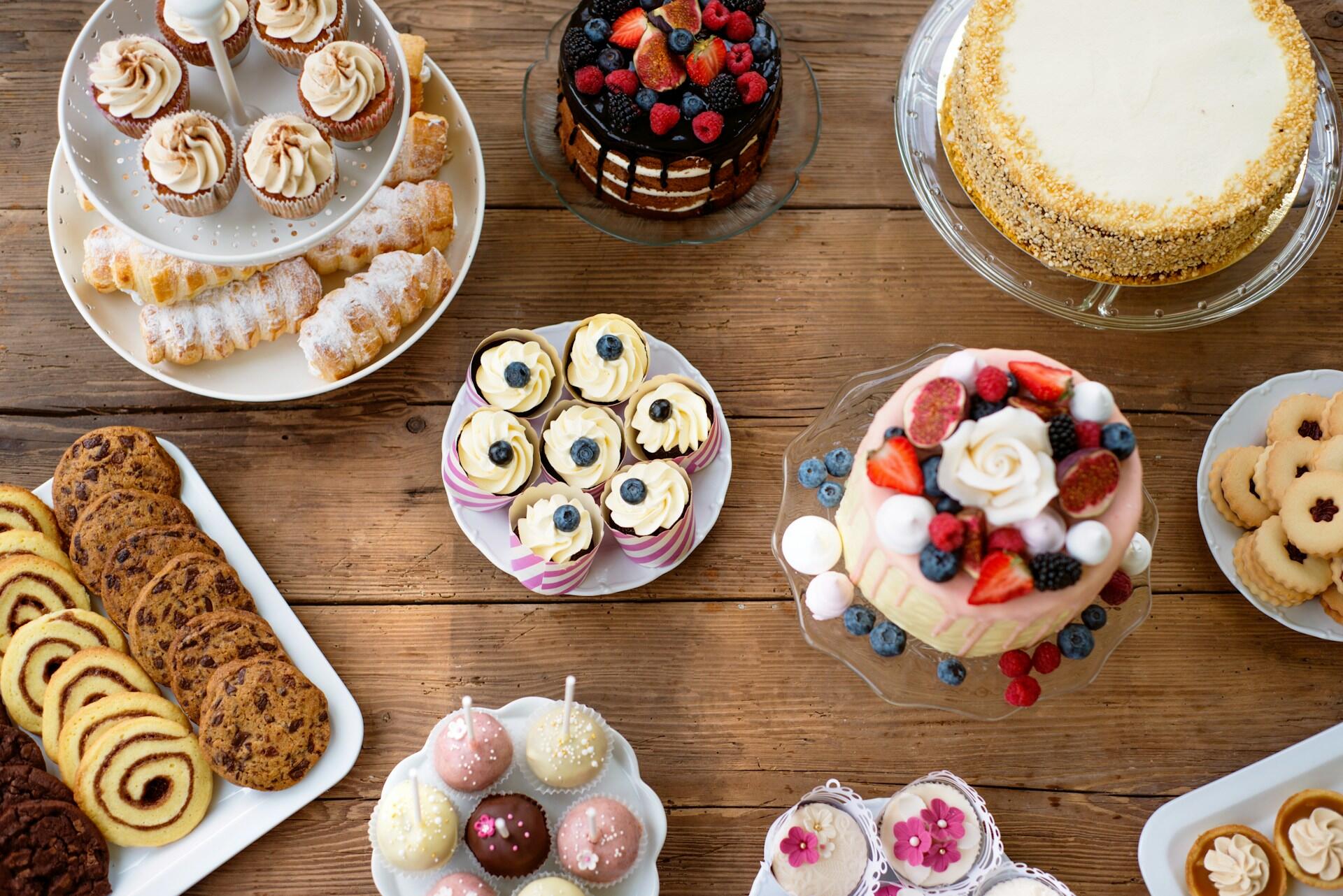 Surtido de postres como tartas, magdalenas, galletas y pasteles en una mesa de madera.