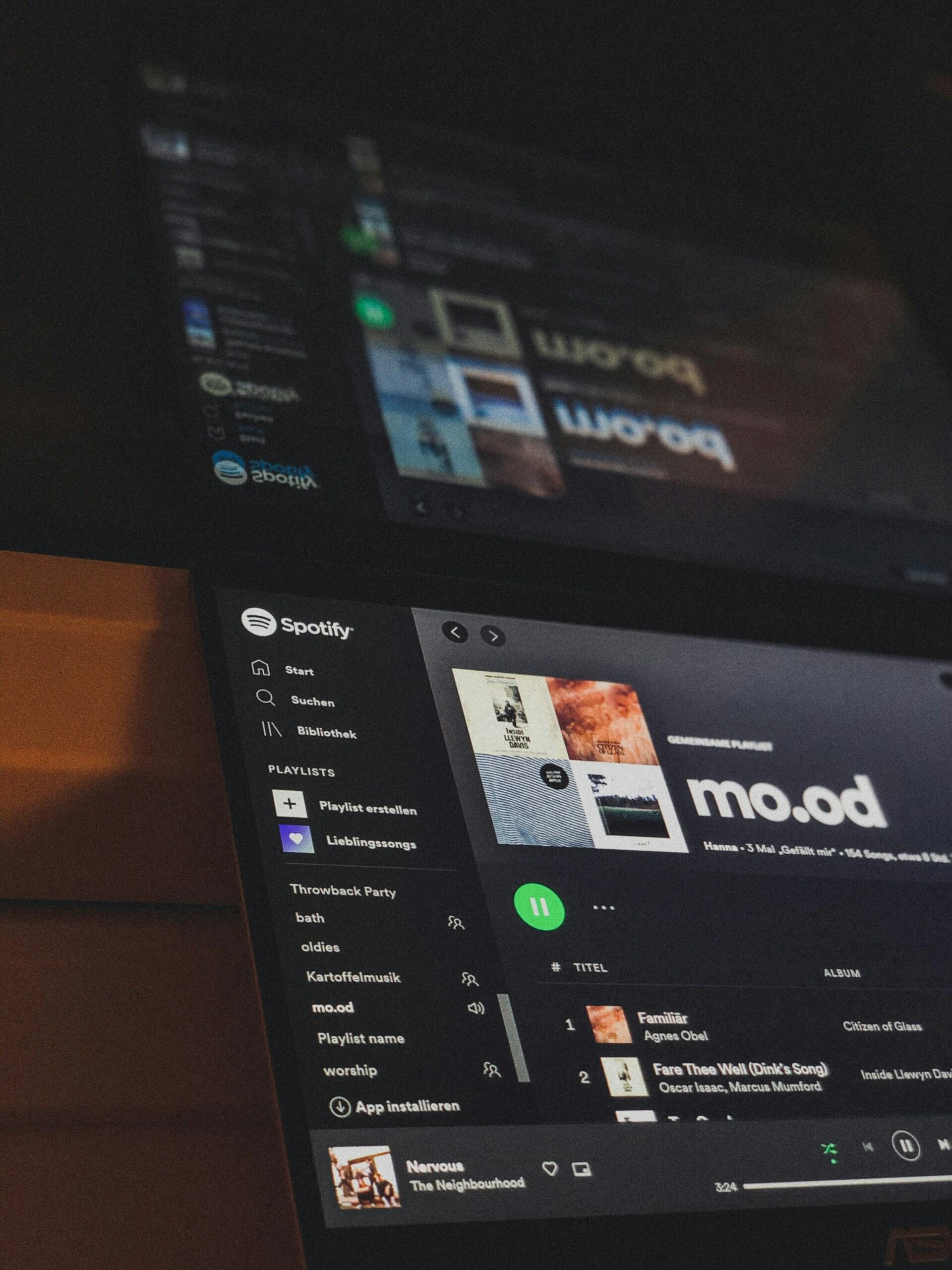 Primer plano de una pantalla de Spotify en la que se muestra una lista de reproducción titulada «mo.od» con la carátula del álbum y la lista de canciones visibles. La escena está tenuemente iluminada, lo que crea un ambiente relajado.