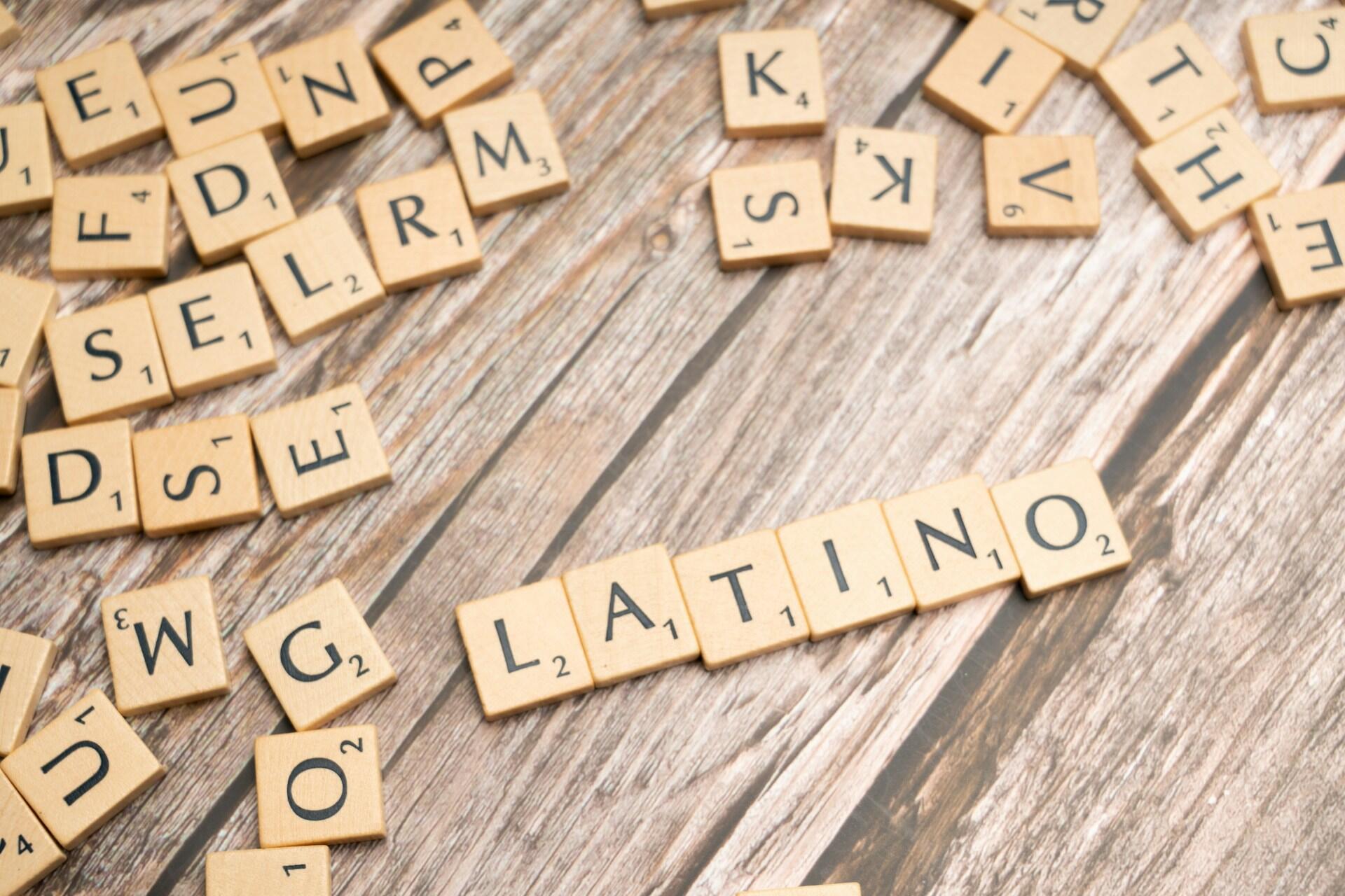 Las fichas de Scrabble esparcidas sobre una superficie de madera forman la palabra «LATINO». Otras letras aleatorias rodean la palabra principal, creando un ambiente divertido y atractivo.