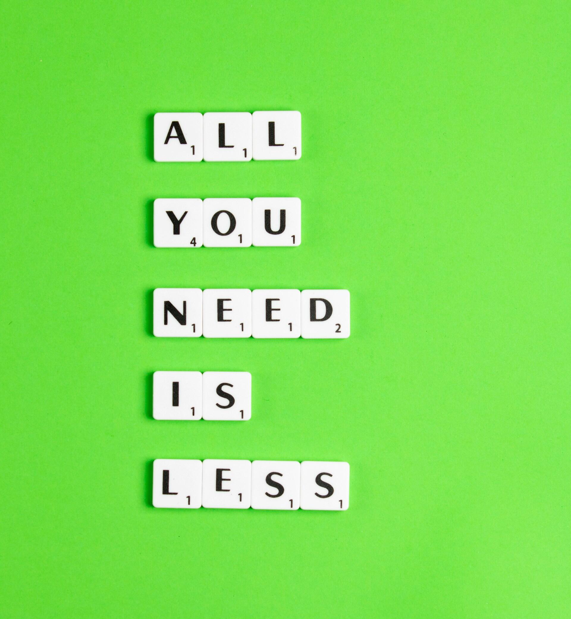 Las fichas de Scrabble, sobre un fondo verde brillante, forman la frase «ALL YOU NEED IS LESS», transmitiendo un mensaje minimalista con sencillez y claridad.