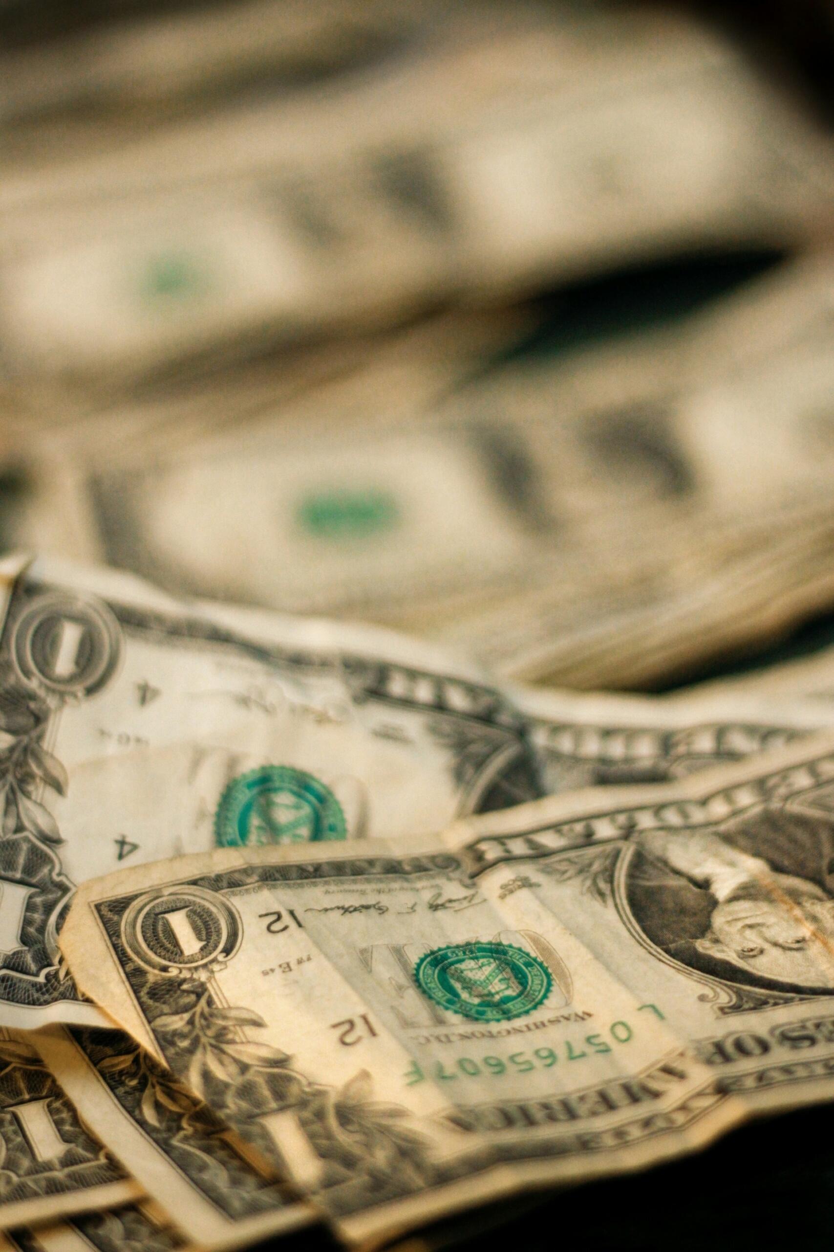 Primer plano de billetes de dólar estadounidense superpuestos, entre los que se incluyen billetes de un dólar, que forman un montón de dinero en efectivo con textura y un tono neutro y financiero.