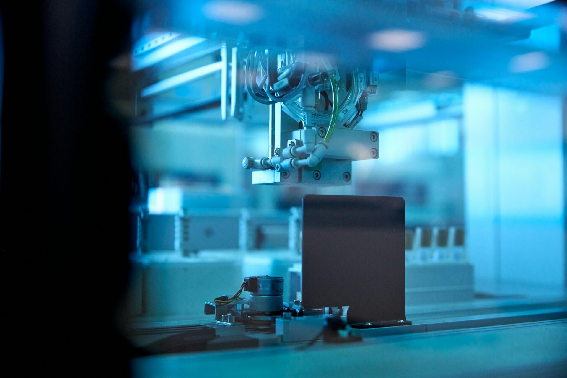 Un brazo robótico, en un laboratorio de alta tecnología, manipula un pequeño componente que refleja la luz azul. La escena transmite precisión y tecnología avanzada.