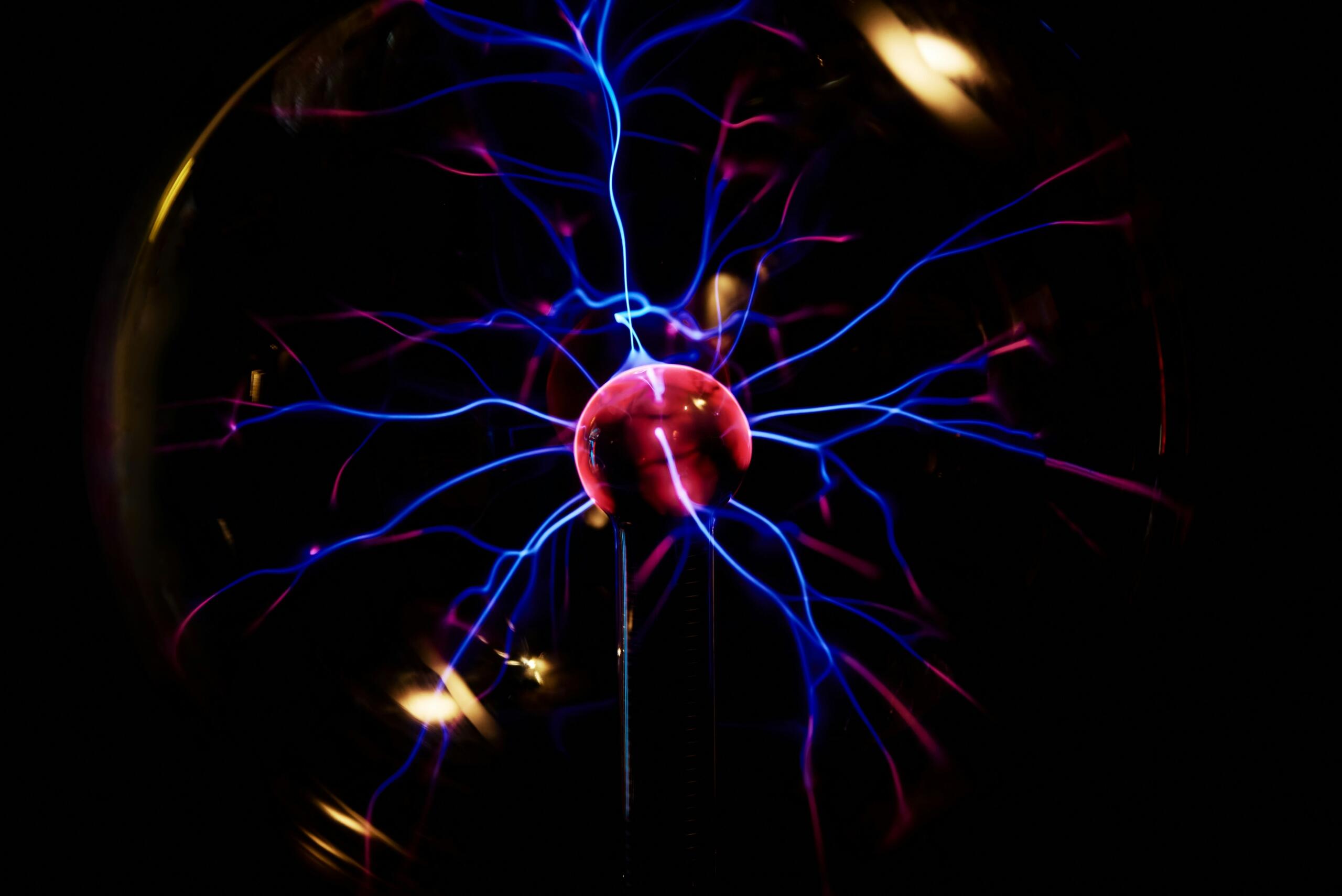 Primer plano de una bola de plasma, en el que se aprecian vibrantes arcos eléctricos azules y rosas que emanan de un orbe luminoso central sobre un fondo oscuro.
