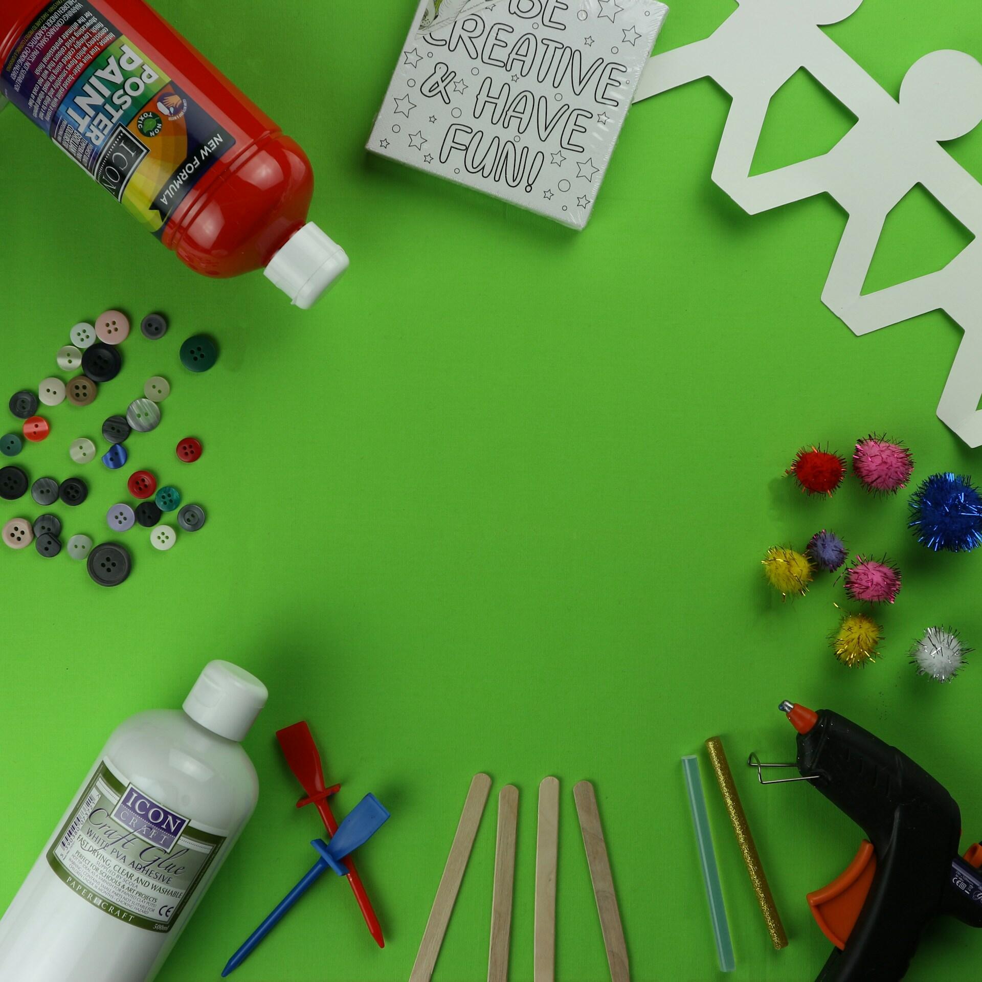 Los materiales de manualidades crean un espacio de trabajo de un verde brillante: pegamento, botones, pompones, palitos de manualidades, pajitas, una pistola de pegamento y un cartel que dice «Sé creativo».