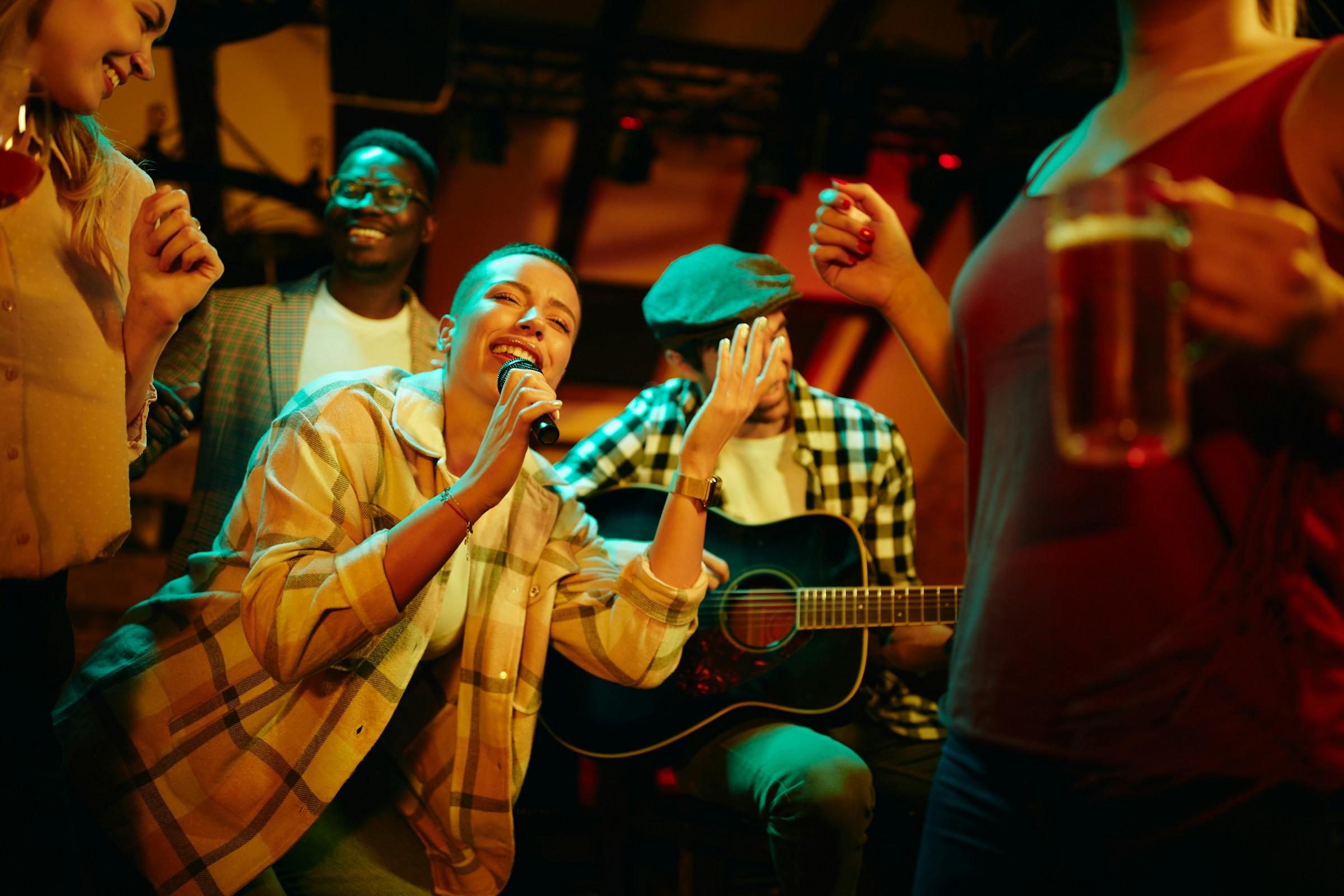 Grupo de personas disfrutando de música en directo en un bar, con un guitarrista y una persona con una cerveza en la mano.
