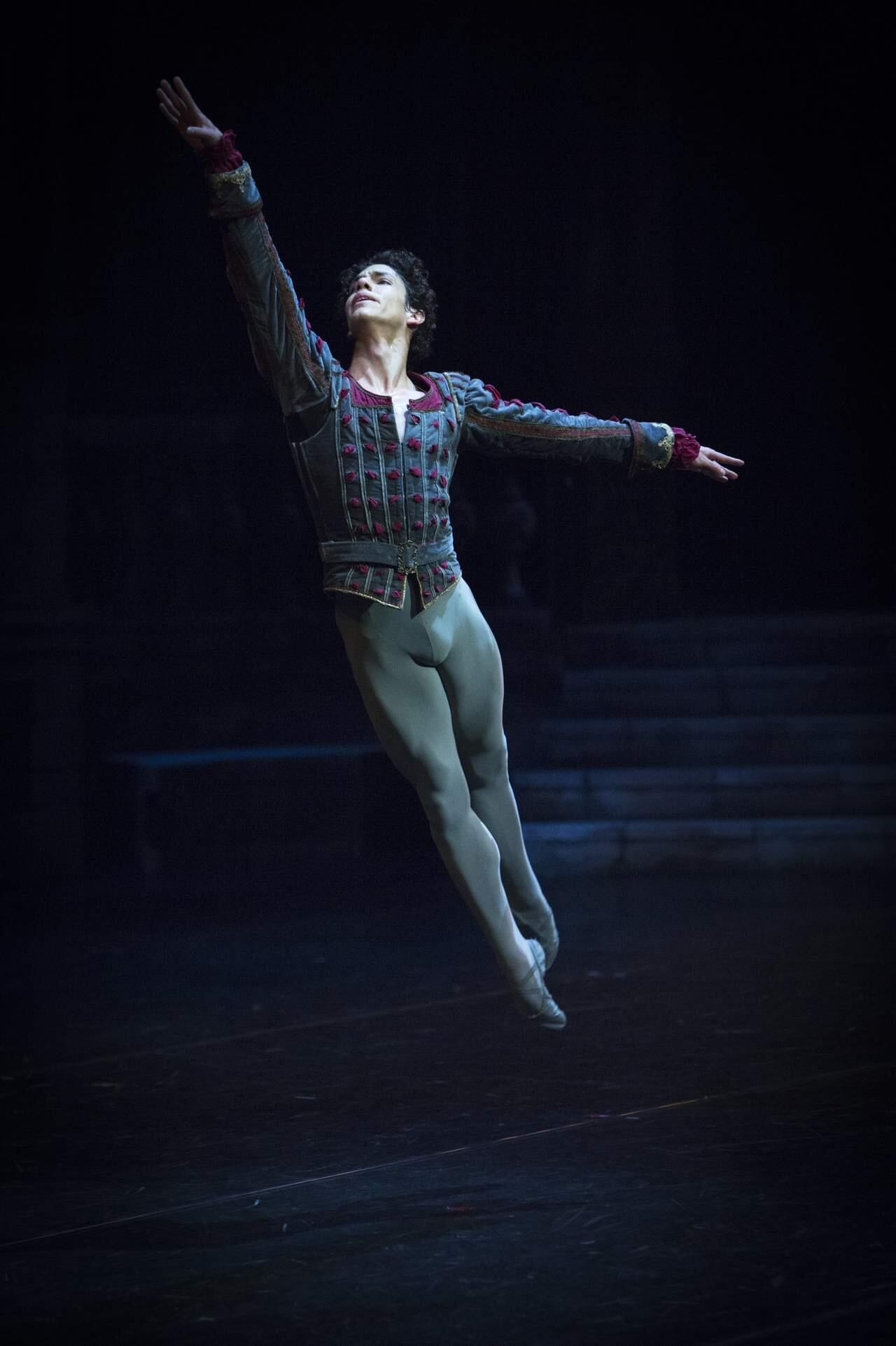 Isaac Hernández con un detallado traje de estilo medieval salta con elegancia en un escenario tenuemente iluminado, transmitiendo elegancia y fuerza.