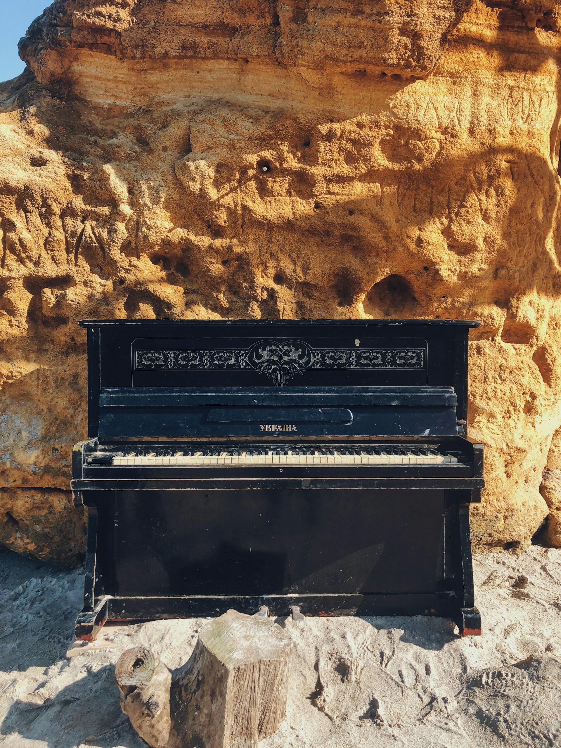 Un piano vertical negro se alza sobre un suelo arenoso, con un acantilado escarpado y bañado por el sol como telón de fondo. El escenario resulta surrealista y contrasta los elementos naturales con los musicales.