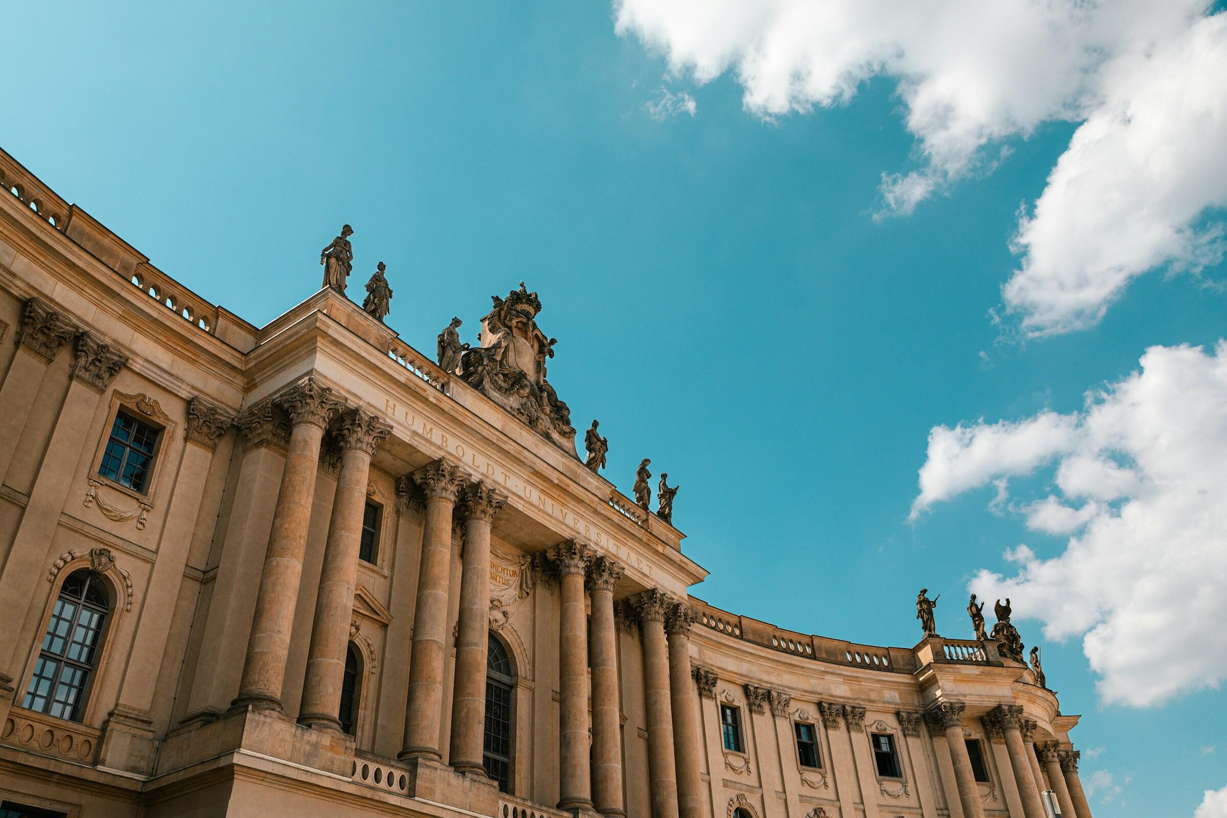 Edificio de la Universidad Humboldt con grandes columnas y esculturas contra un cielo azul brillante, que muestra una arquitectura clásica.