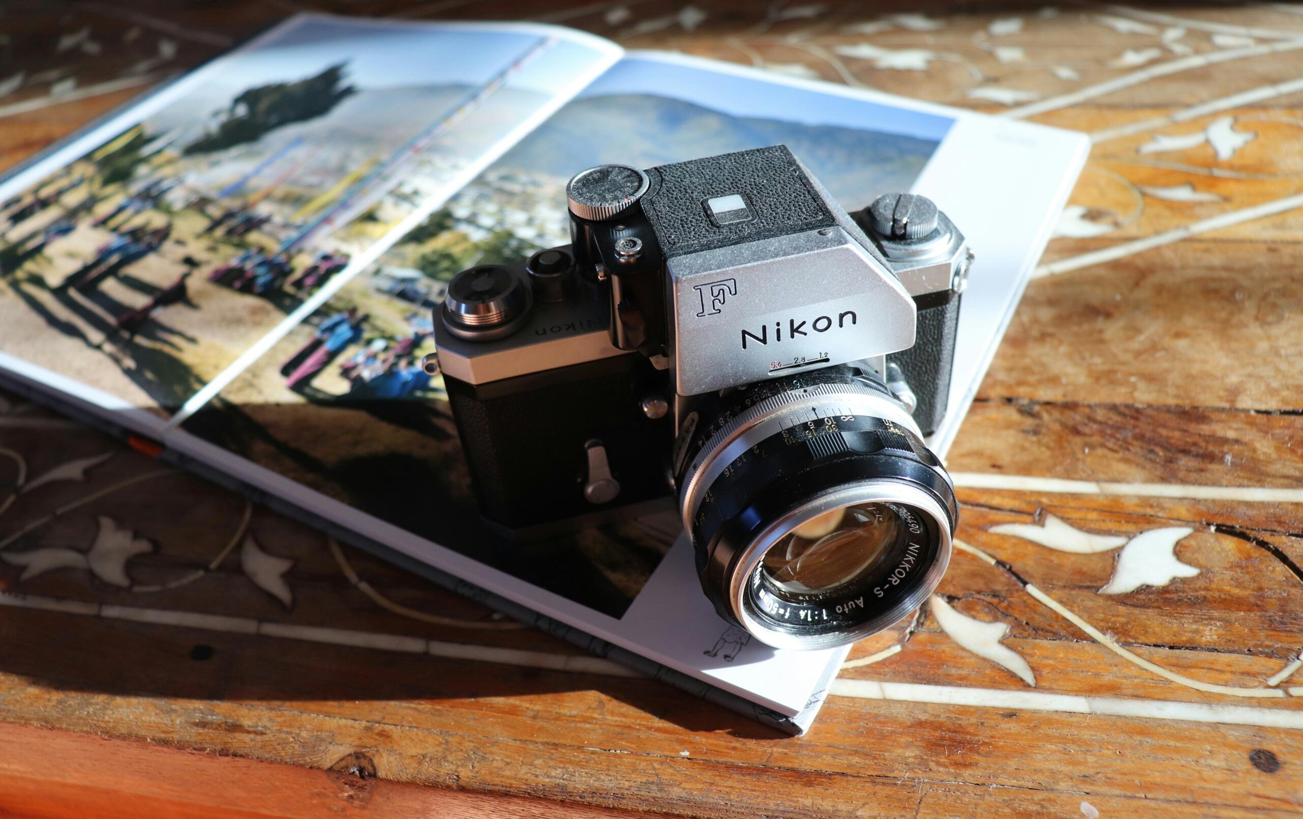 Cámara Nikon F de época apoyada sobre un álbum de fotos abierto con imágenes al aire libre, colocado sobre una mesa de madera con incrustaciones decorativas.