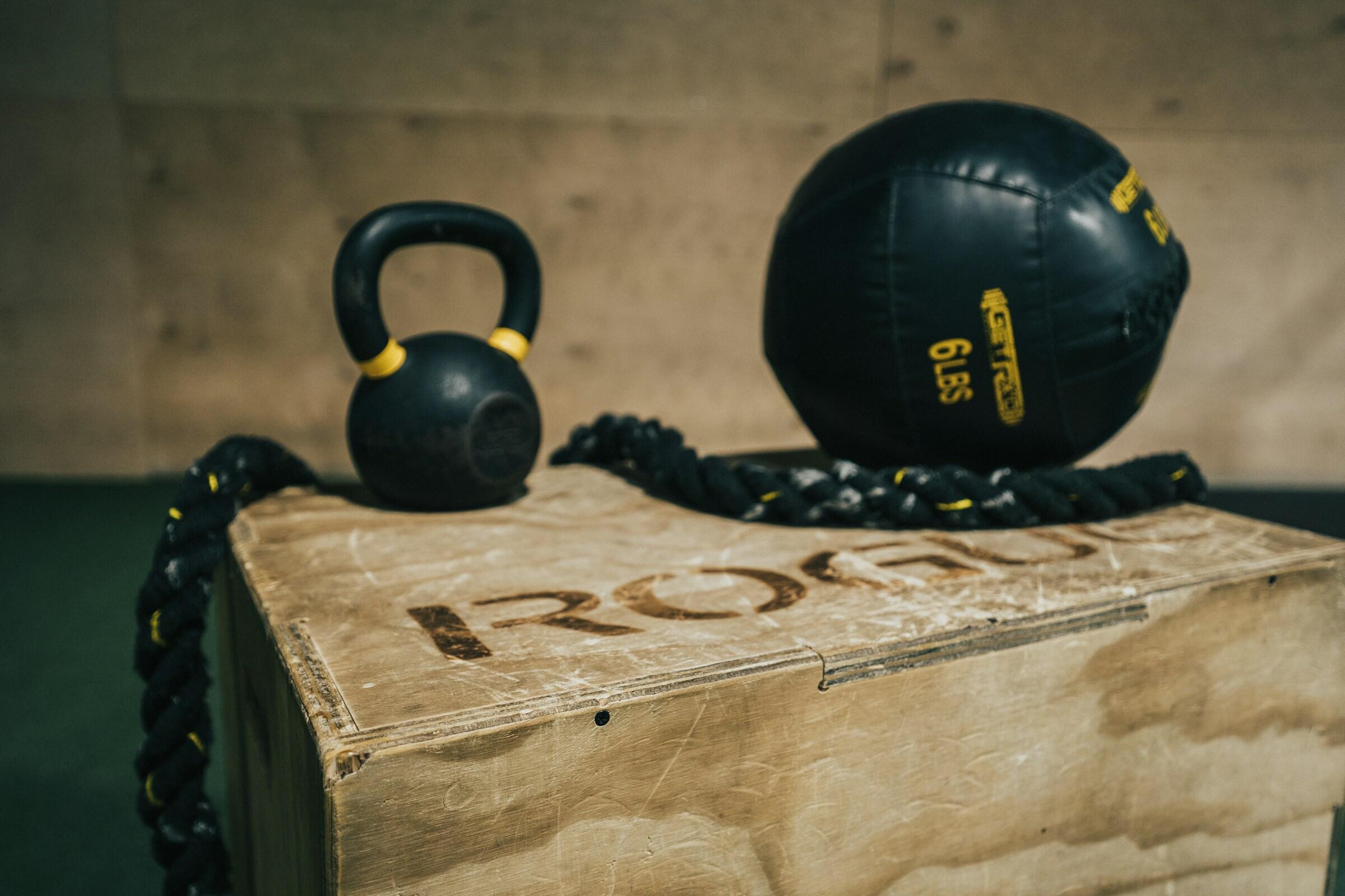 Una kettlebell, una cuerda pesada y un balón medicinal en una caja de entrenamiento de madera.