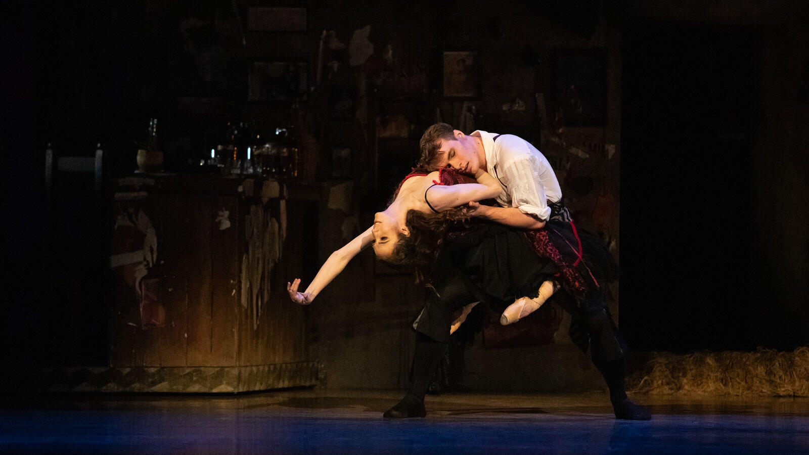 Los bailarines actúan con pasión sobre el escenario, y la tenue iluminación realza sus poses expresivas. El fondo está suavemente iluminado, lo que crea una atmósfera dramática.
