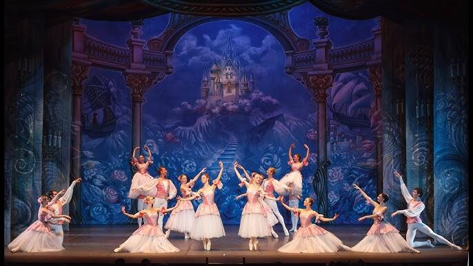 Bailarines de ballet con trajes rosas y blancos actúan con elegancia sobre el escenario. Un caprichoso decorado de castillo realza el ambiente encantador y de cuento de hadas.