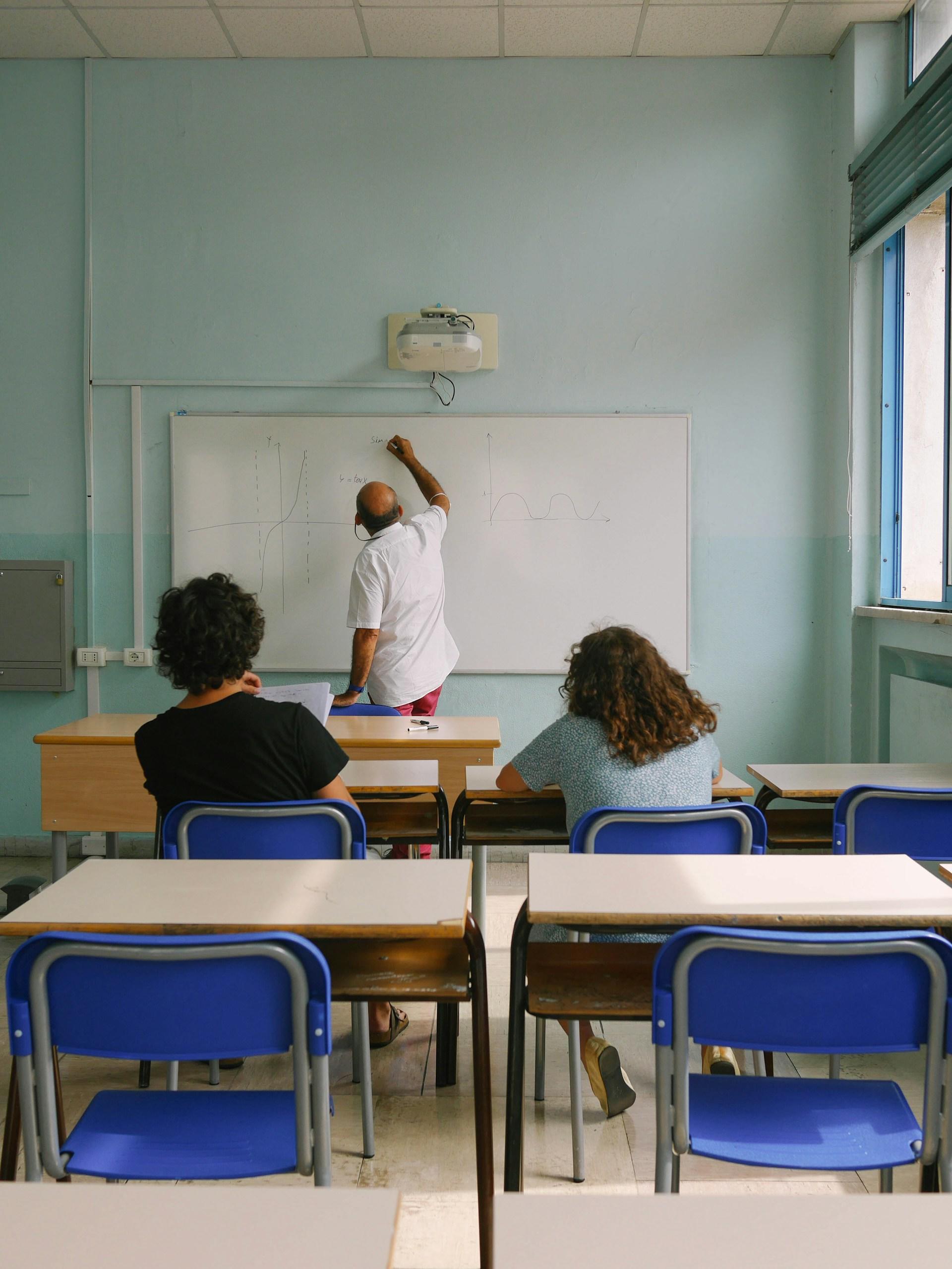 profesor dando clases de matematicas a dos alumnos en una sala