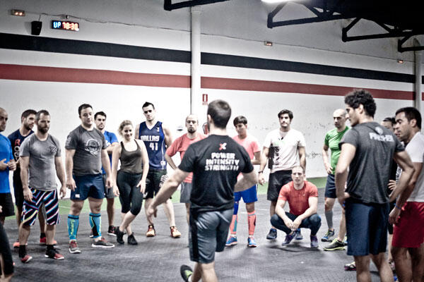 Un grupo de personas vestidas con ropa deportiva se reúne alrededor de un entrenador en un gimnasio. Sus expresiones concentradas, su ropa de colores vivos y su postura dinámica crean un ambiente lleno de energía.