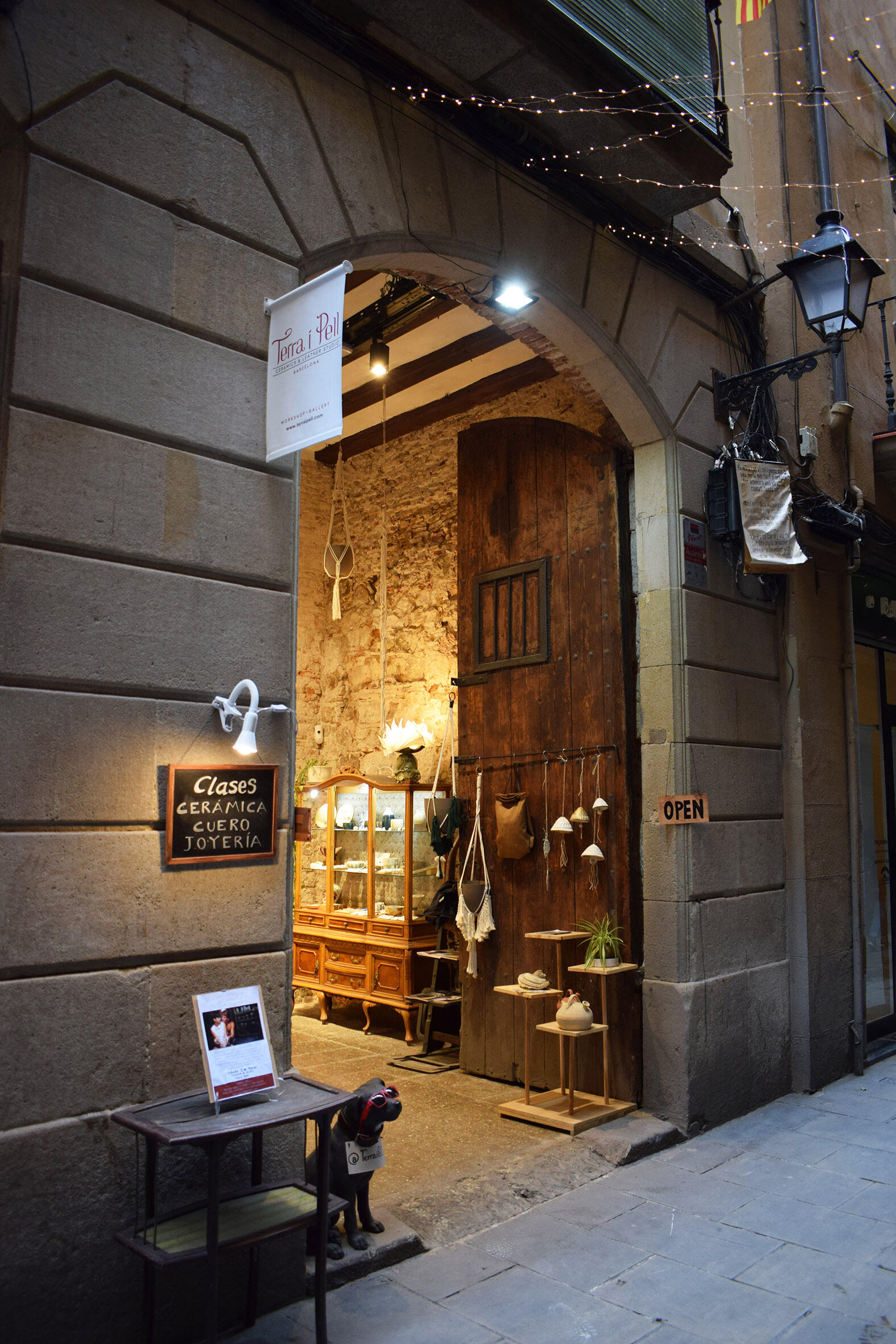 Entrada encantadora a una tienda artesanal con puertas de madera, expositores vintage y una simpática estatua de un perro con gafas de sol. Cartel de «Abierto» visible.
