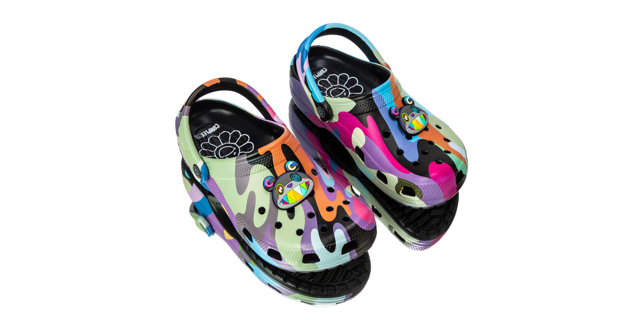 Zuecos coloridos con diseño de dibujos animados, con un estampado caprichoso de pintura chorreada y detalles multicolores. Una cara de personaje alegre y vibrante decora la parte superior.