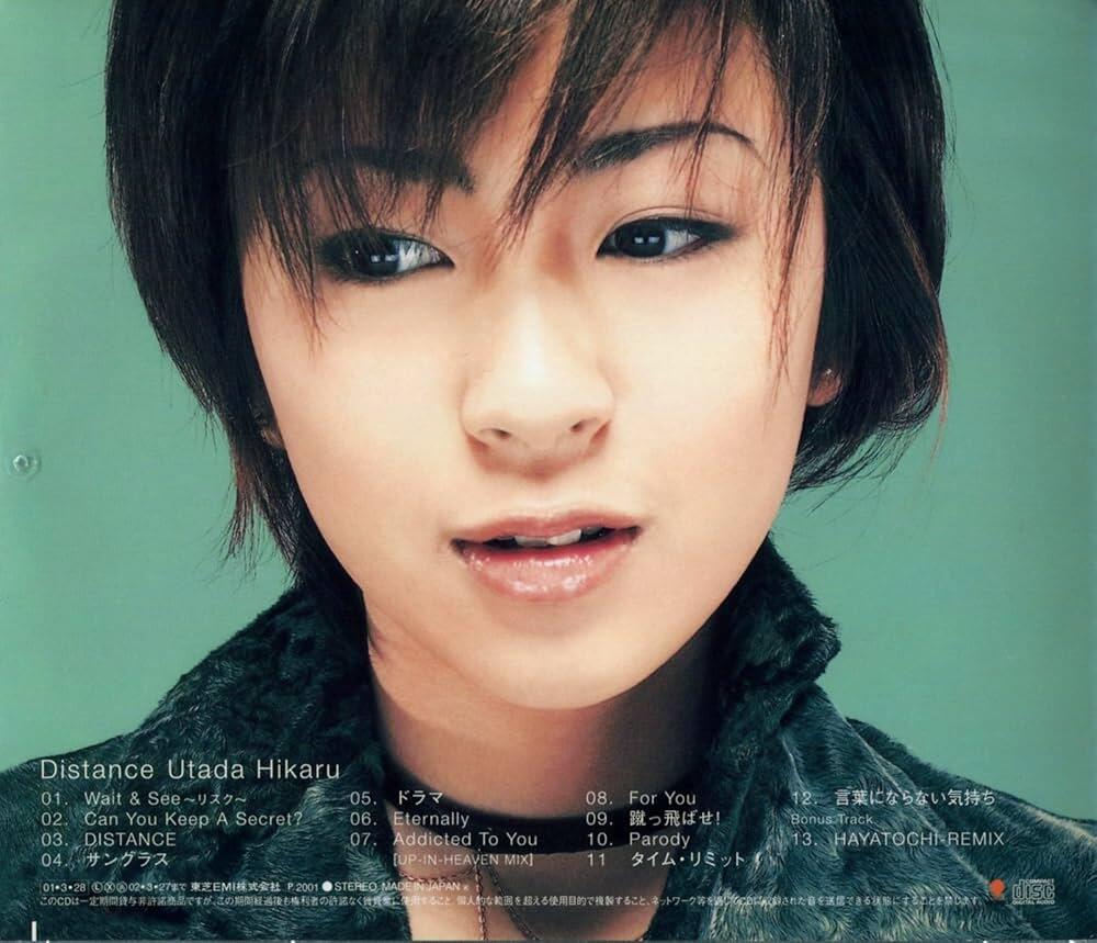 Primer plano de una persona con cabello castaño corto, sonriendo suavemente sobre un fondo verde azulado. Lleva una chaqueta oscura con textura. El texto debajo enumera canciones.