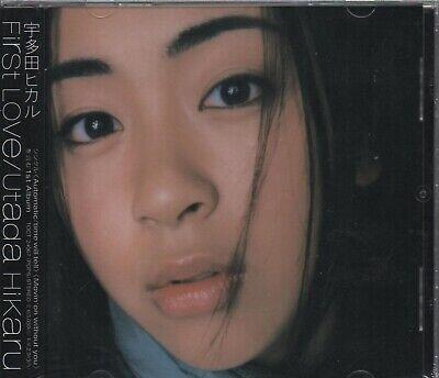 Primer plano del rostro de una persona con cabello largo y oscuro y ojos expresivos. La mirada es tranquila y contemplativa. El círculo de texto en la esquina dice: «Primer amor Utada Hikaru».