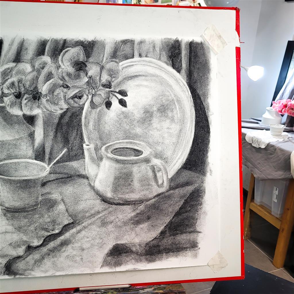 Naturaleza muerta en carboncillo de una tetera, un plato y una taza con cuchara, sobre un fondo de tela drapeada y flores. La escena crea un ambiente tranquilo y clásico.