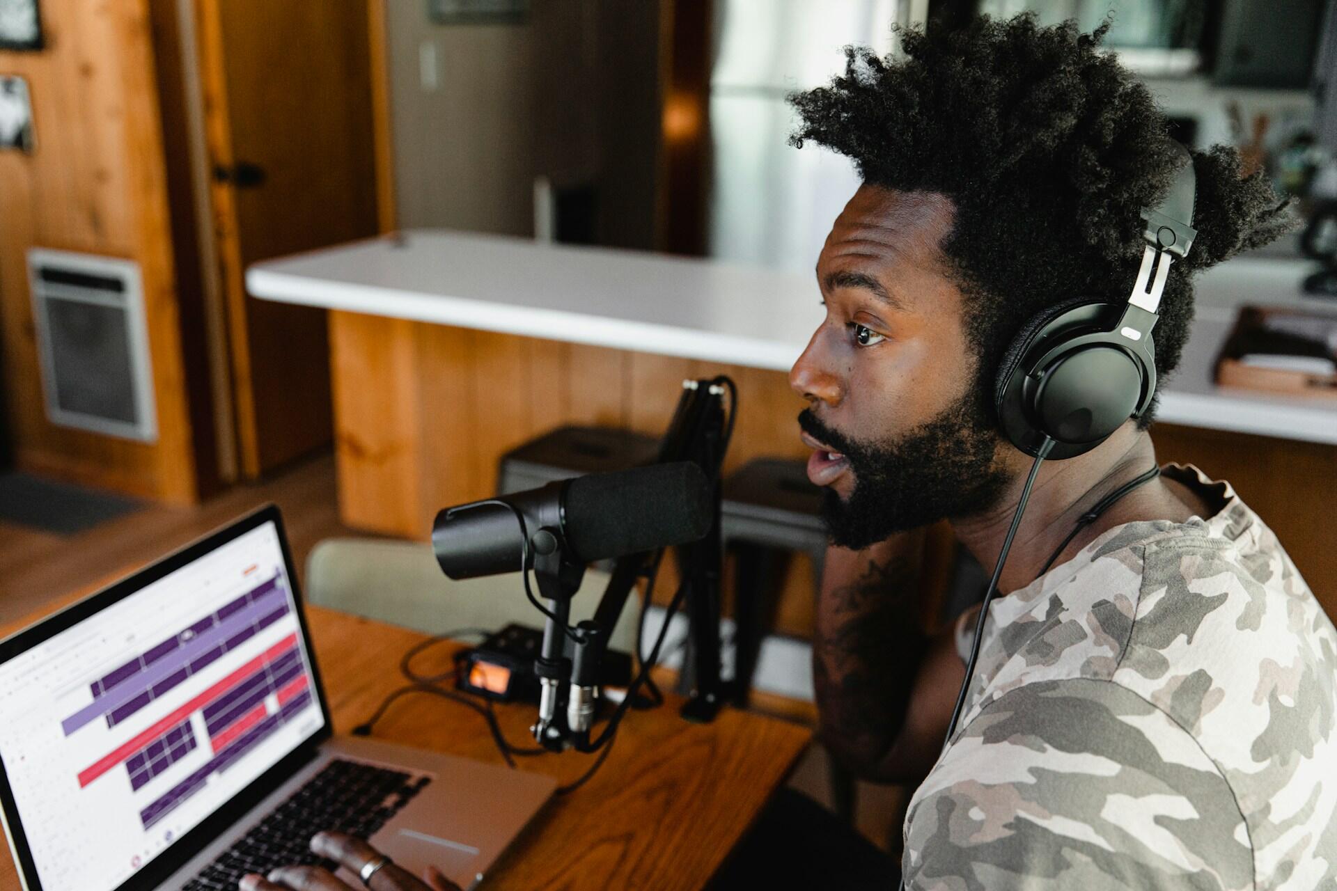Una persona que usa auriculares mira fijamente a una computadora portátil con un software de edición de audio, ubicada en un acogedor espacio interior de madera.