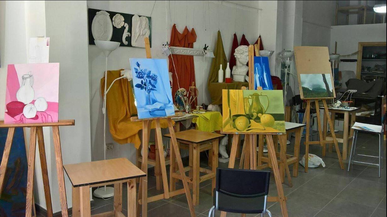 Estudio de arte lleno de caballetes con coloridos bodegones; estatuas y telas vibrantes al fondo crean una atmósfera creativa e inspiradora.