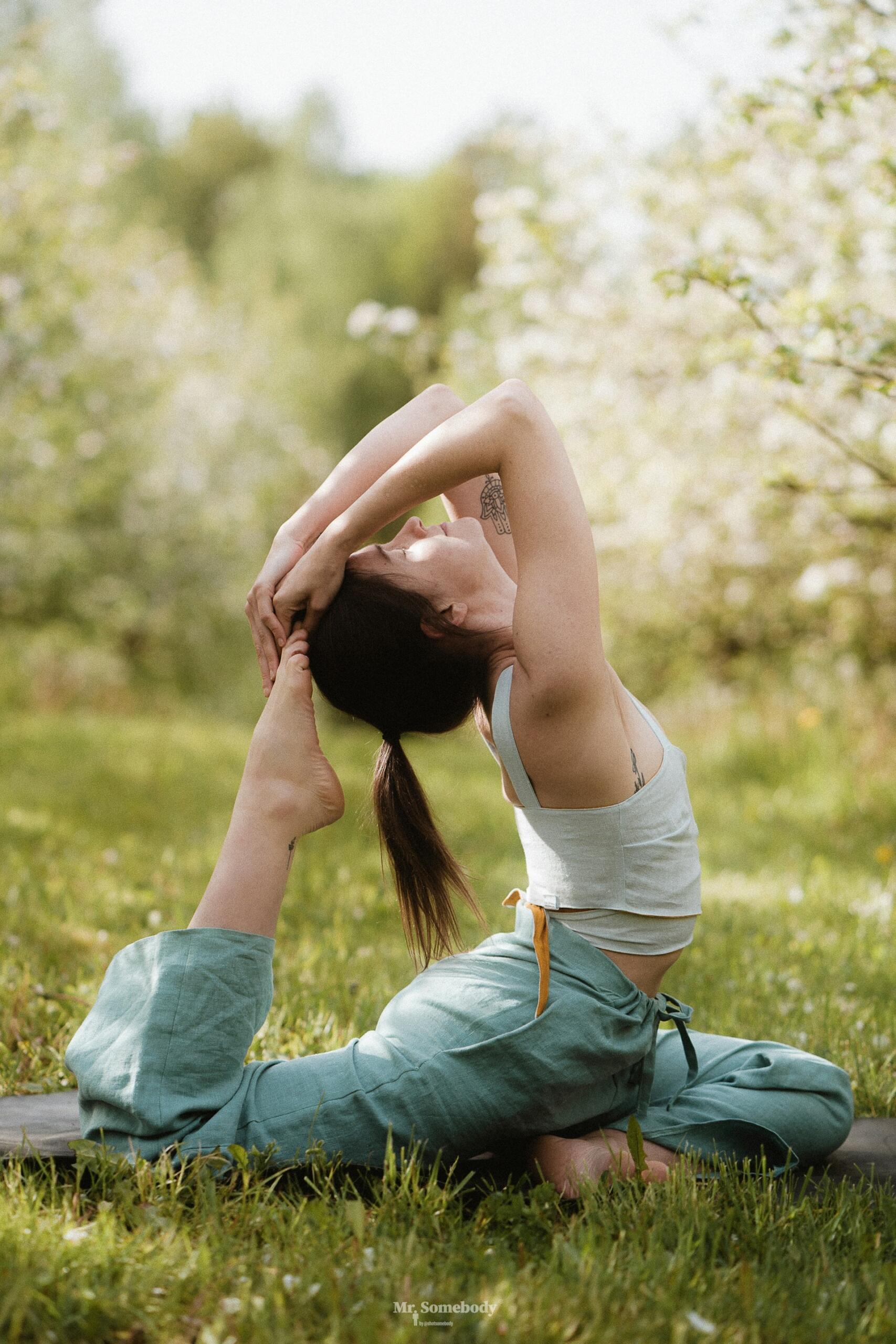 Una persona practica yoga al aire libre en un entorno verde y frondoso, realizando una elegante flexión hacia atrás con una pierna extendida. La escena transmite tranquilidad y concentración.