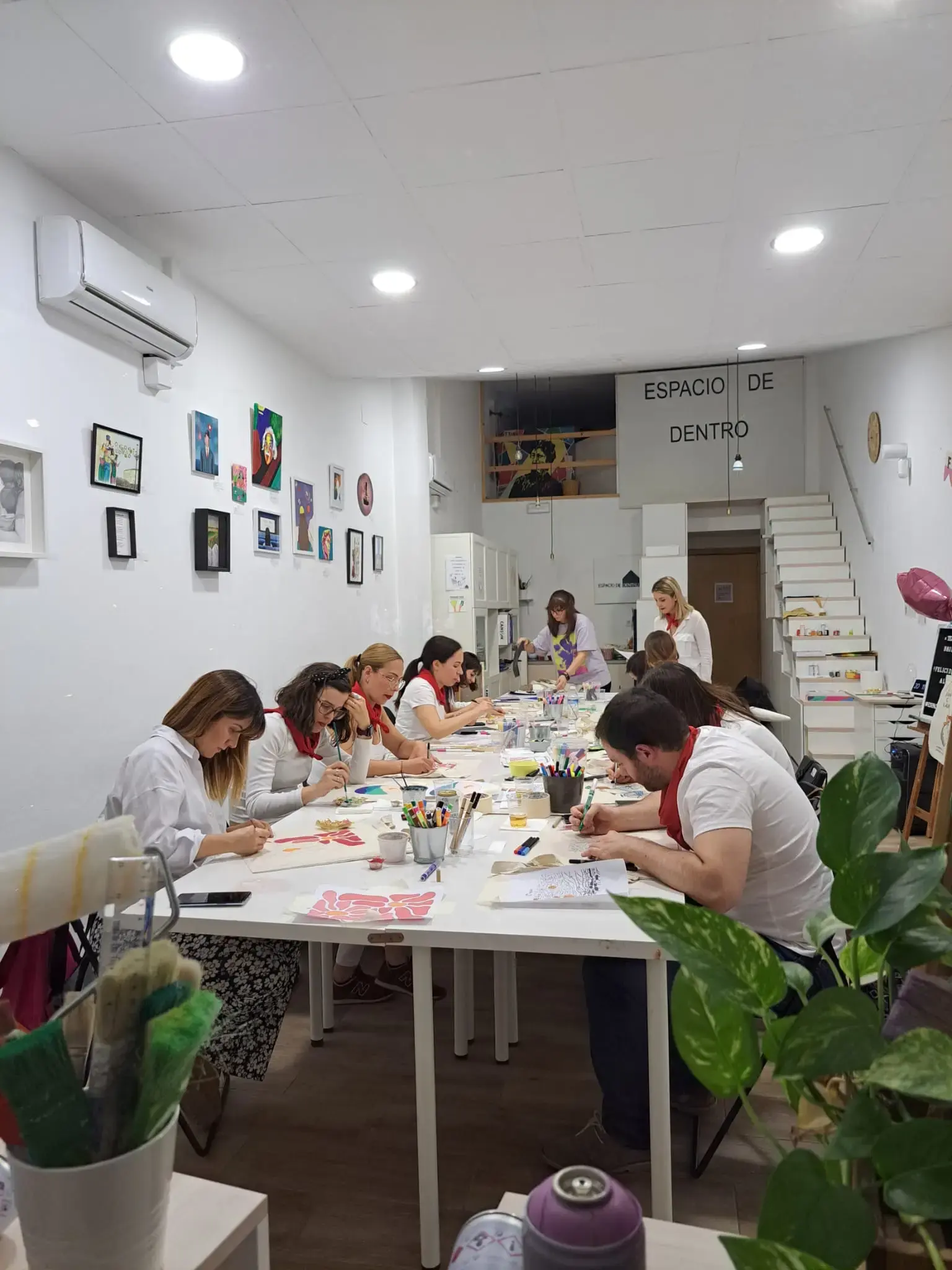 Una escena de taller creativo con participantes concentrados en pintar en un estudio luminoso, rodeados de obras de arte y materiales artísticos.