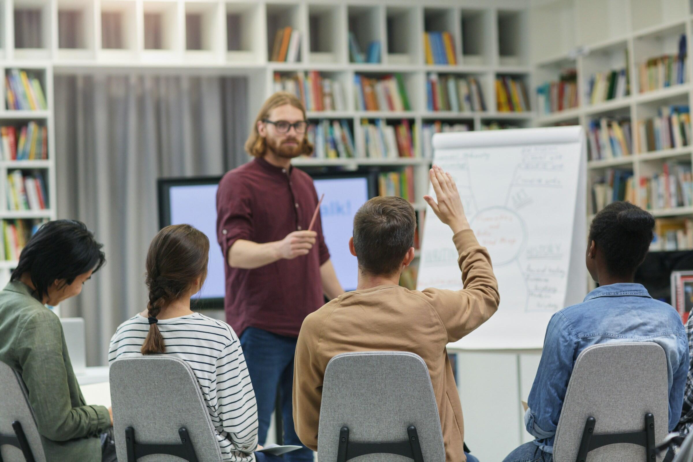 Un grupo de personas participando en un taller, con un presentador dirigiéndose al público y una pizarra llena de notas al fondo.