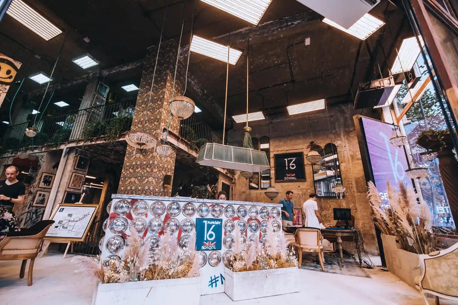 Interior de una cafetería moderna con decoración industrial, en el que destaca una gran barra adornada con esferas reflectantes. Las plantas en macetas aportan un toque de verdor. La iluminación cálida crea un ambiente acogedor.