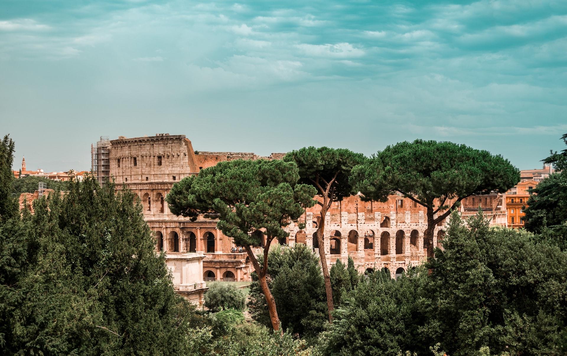 Una postal del coliseo tras los árboles en Roma