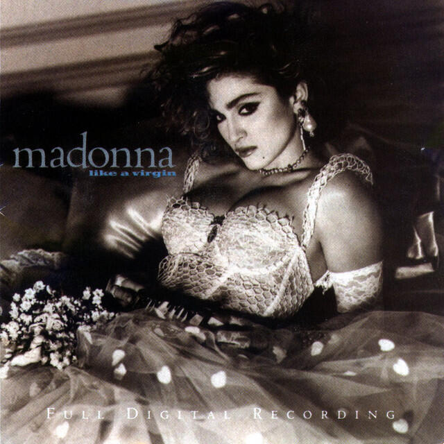 Imagen en blanco y negro de Madonna vestida con encaje tumbada en una cama, con una expresión segura y provocativa. El texto dice «Madonna Like a Virgin».
