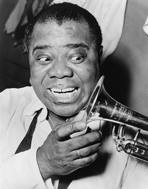 Un Louis Armstrong sonriente con una trompeta cerca de la cara, vestido con una camisa blanca y corbata oscura. El ambiente es alegre y expresivo, y transmite entusiasmo y pasión por la música.