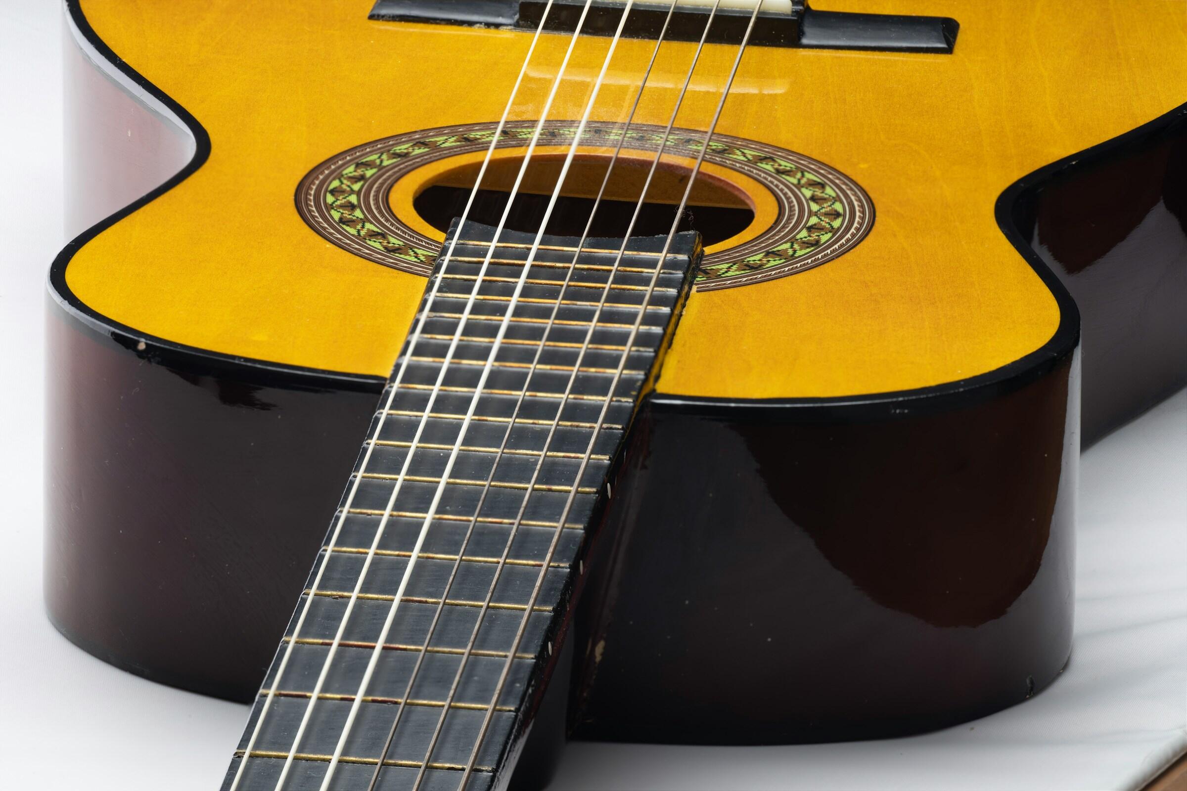 Primer plano de una guitarra acústica en el que se aprecian el mástil, la boca con su roseta decorativa y el cuerpo amarillo y negro.
