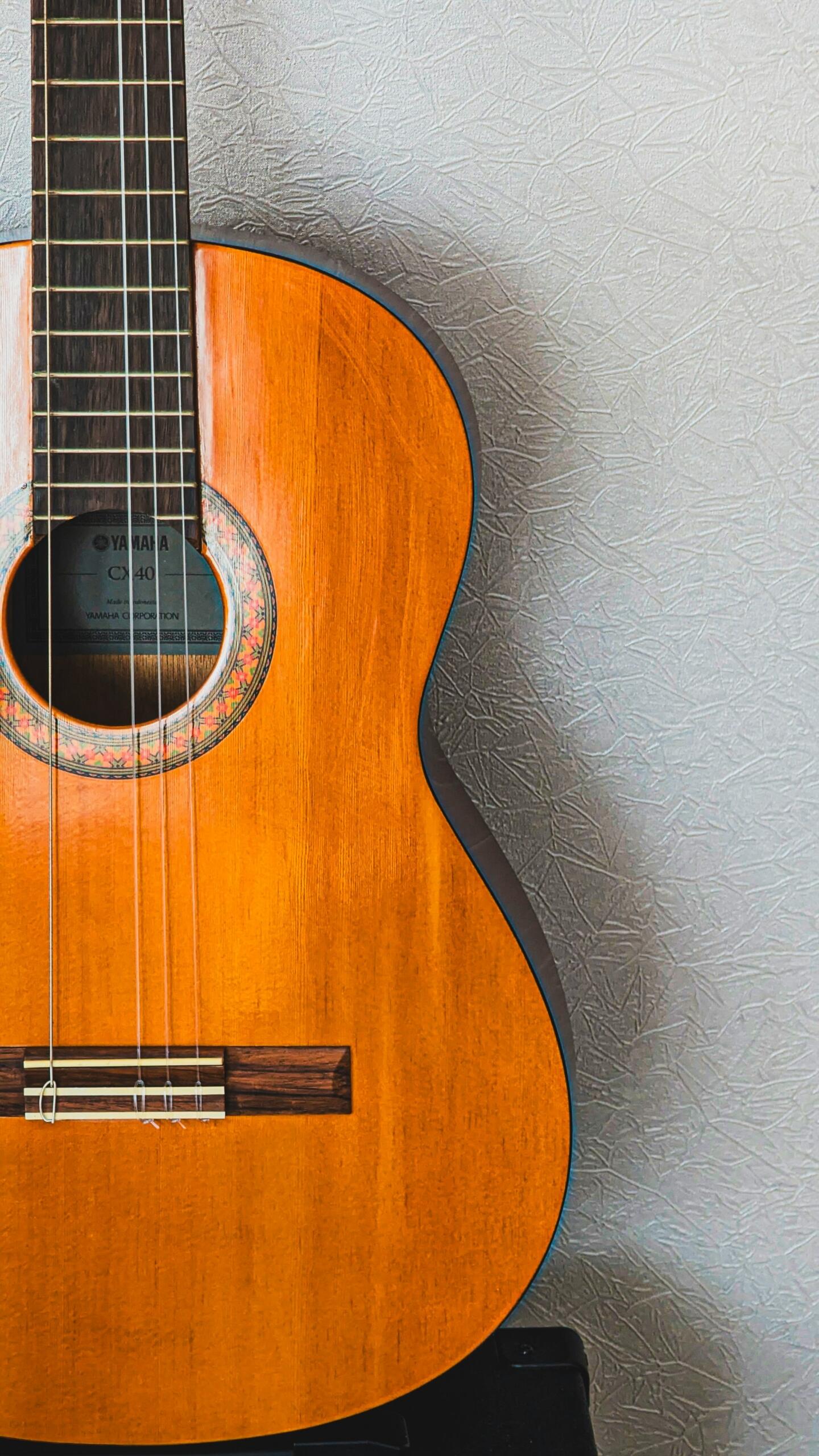 Primer plano de una guitarra acústica de color marrón anaranjado sobre un fondo de pared gris claro con textura.