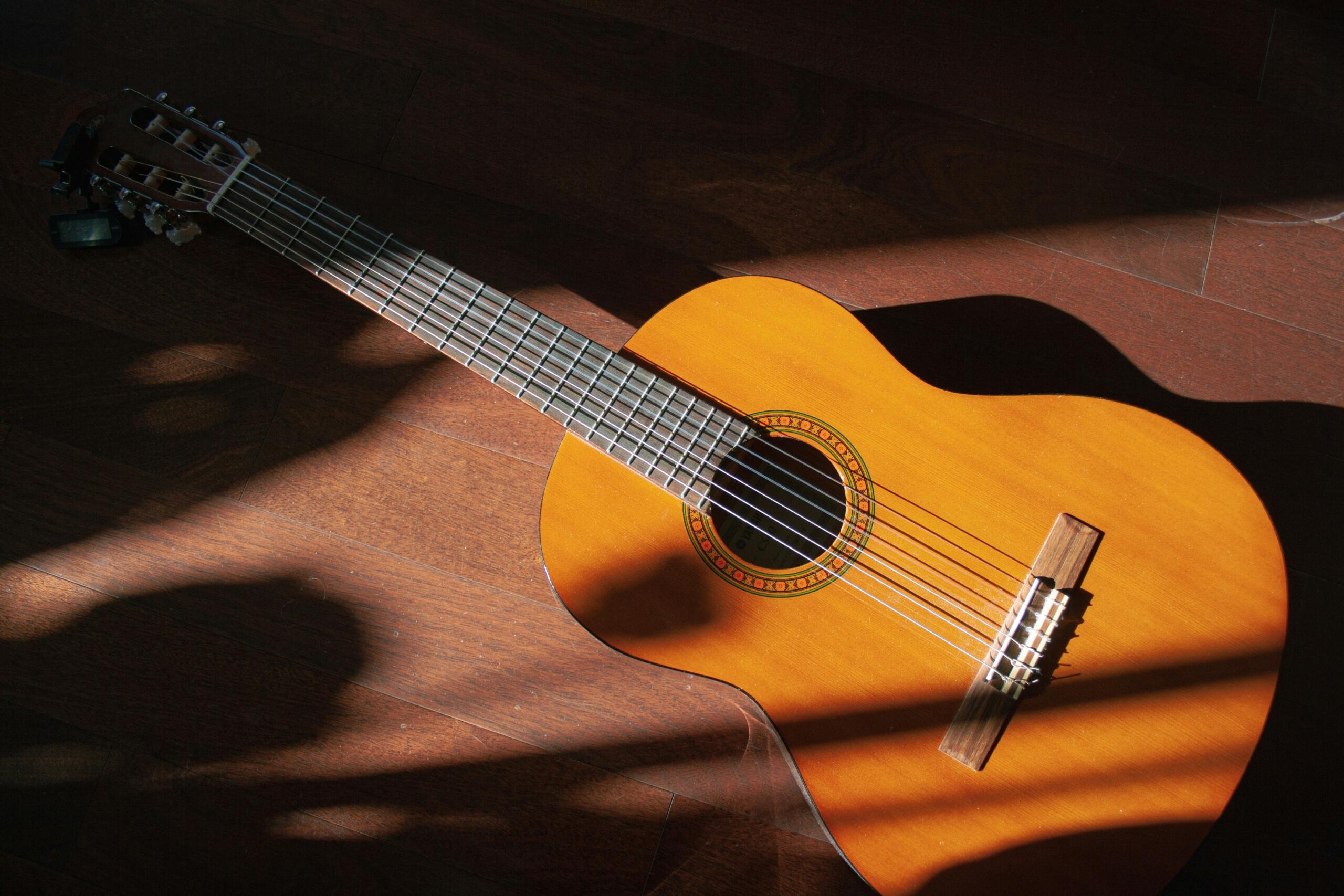 Una guitarra acústica sobre un suelo de madera, con la luz del sol y los juegos de sombras proyectándose sobre él.