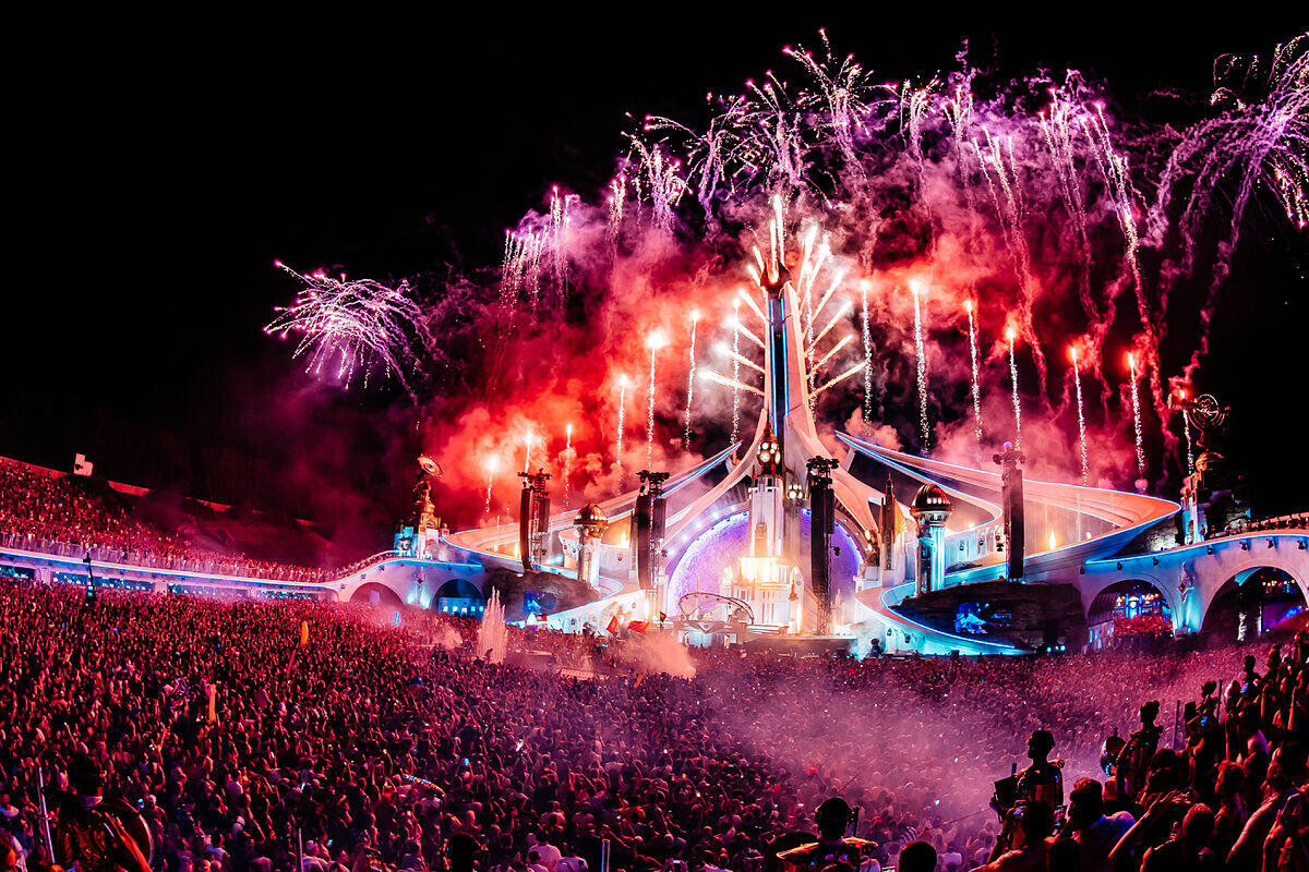 Un vibrante festival de música con una gran multitud, un gran escenario iluminado y coloridos fuegos artificiales en el cielo nocturno, creando una atmósfera electrizante.
