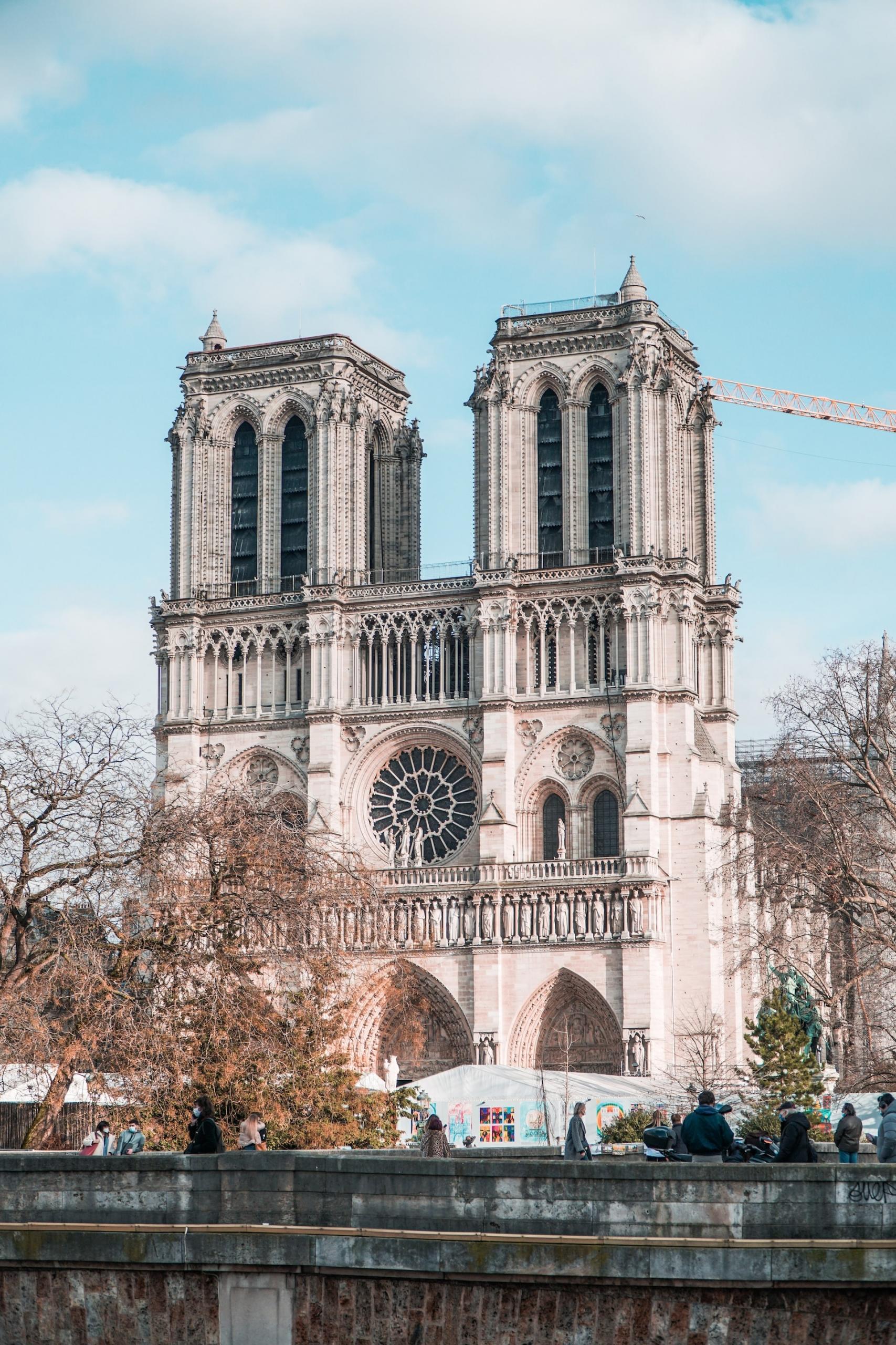 La emblemática catedral de Notre-Dame se eleva sobre los visitantes, mostrando su intrincada arquitectura y su rosetón bajo un cielo azul claro.