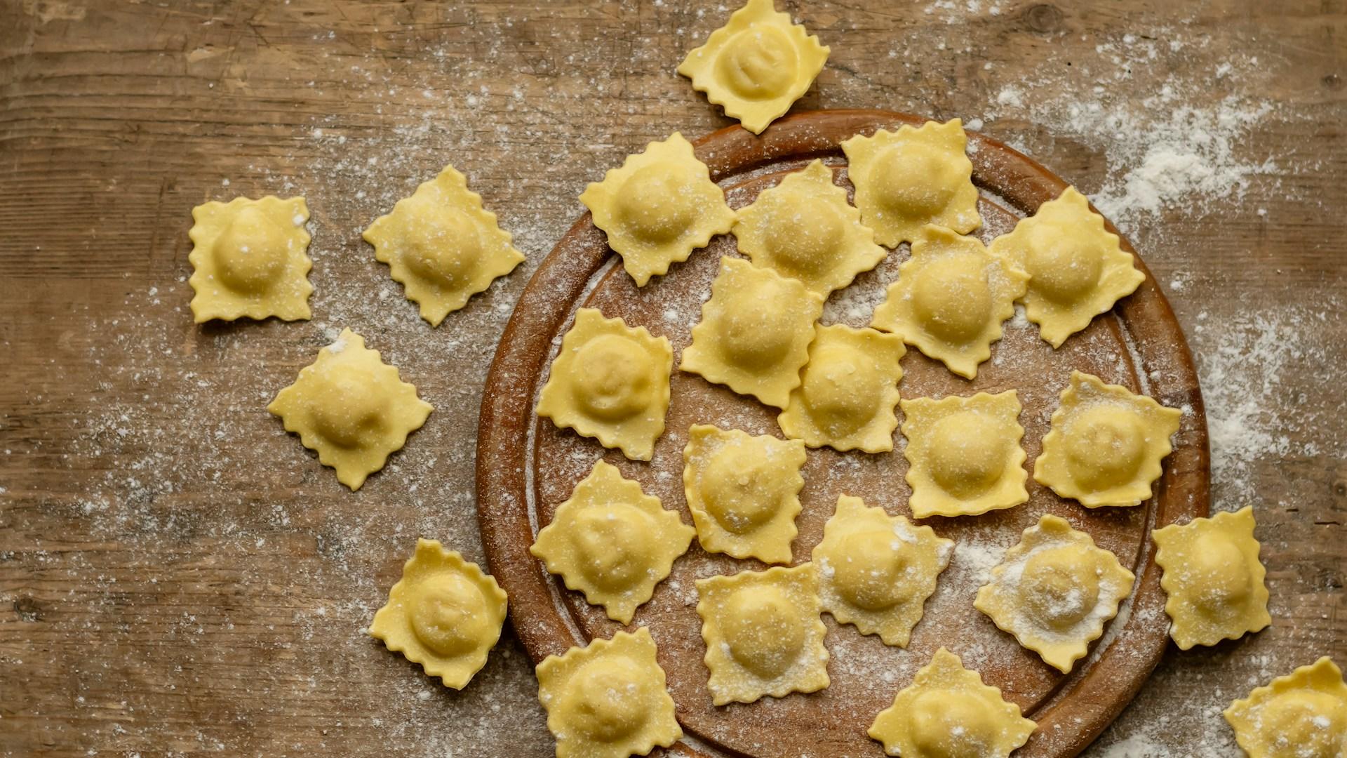 Pasta fresca para raviolis con harina sobre tabla y mesa de madera.