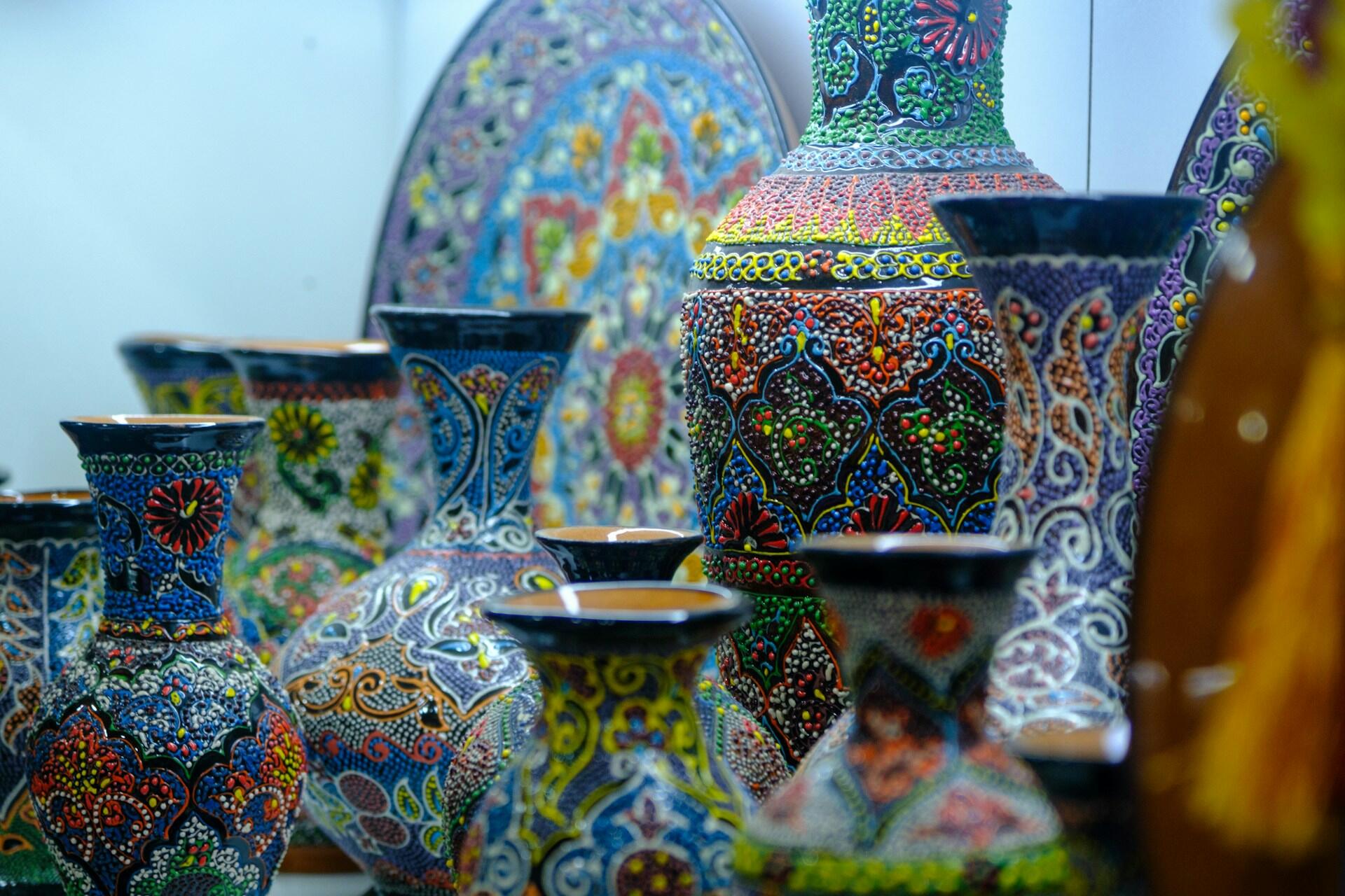 Los jarrones y platos de cerámica, pintados con colores vivos y motivos intrincados, muestran diseños coloridos y detallados. La escena transmite una sensación de arte y riqueza cultural.