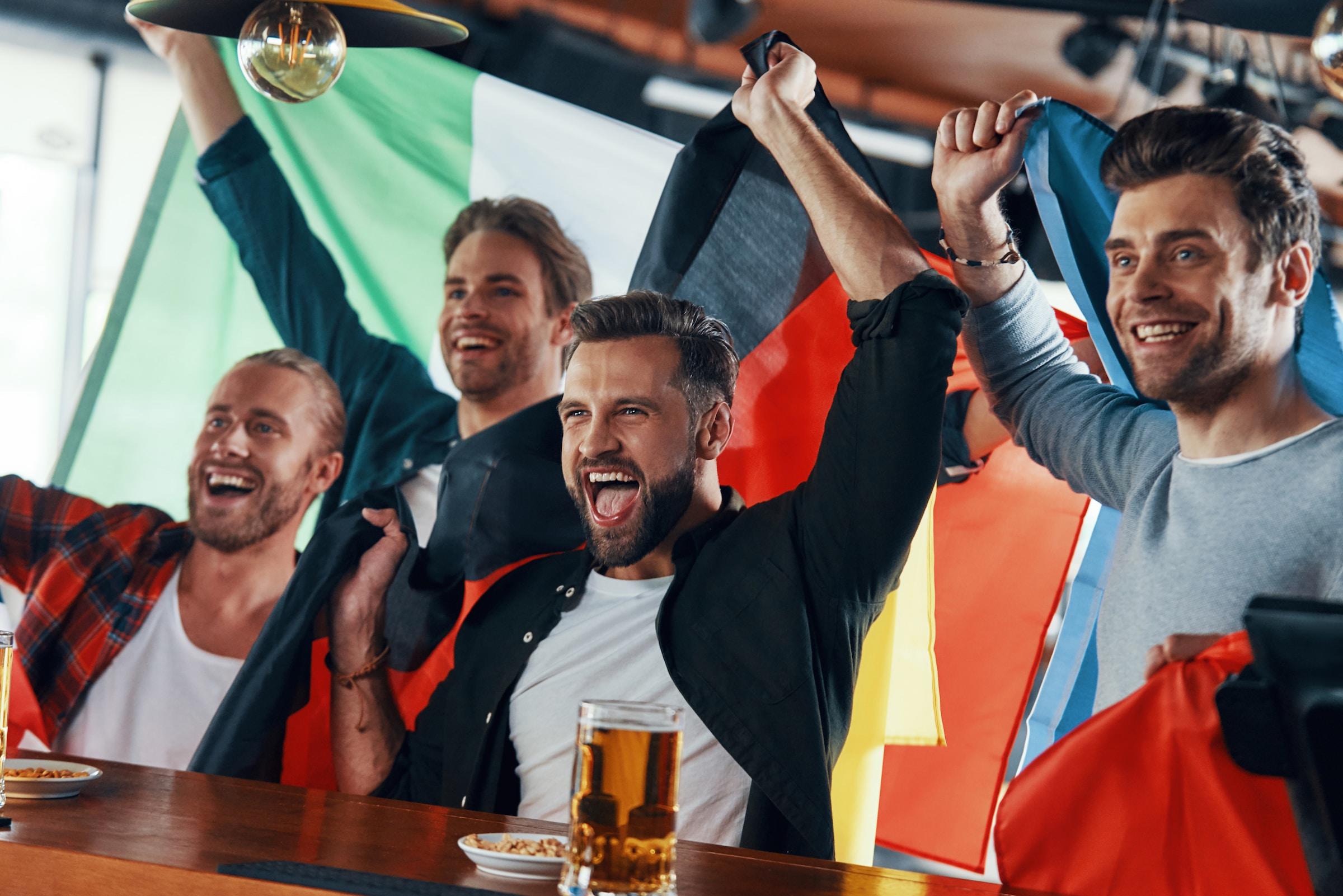 amigos celebrando un gol con banderas y cerveza en la barra
