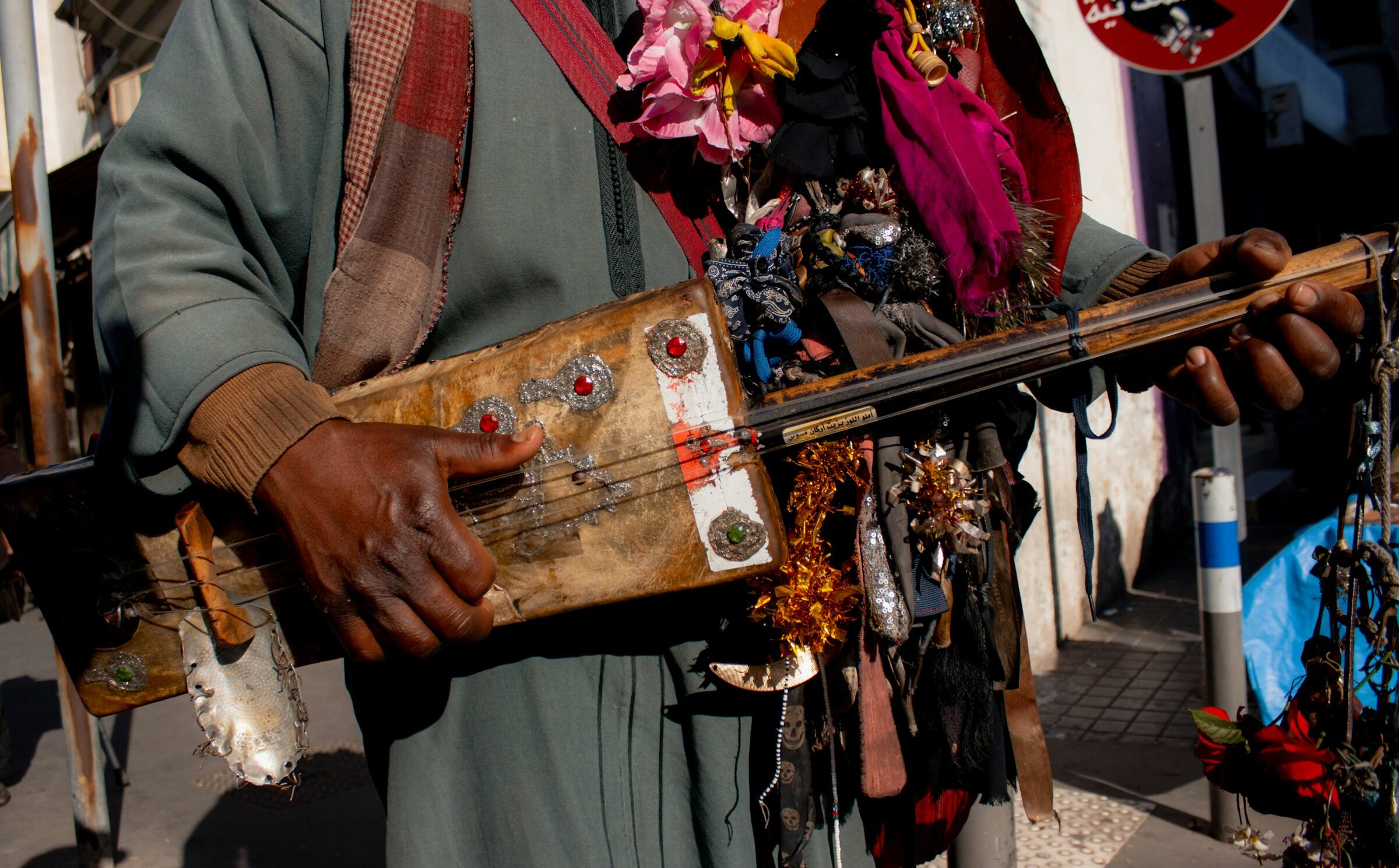 Primer plano de una persona tocando un instrumento de cuerda tradicional decorado en una calle soleada.