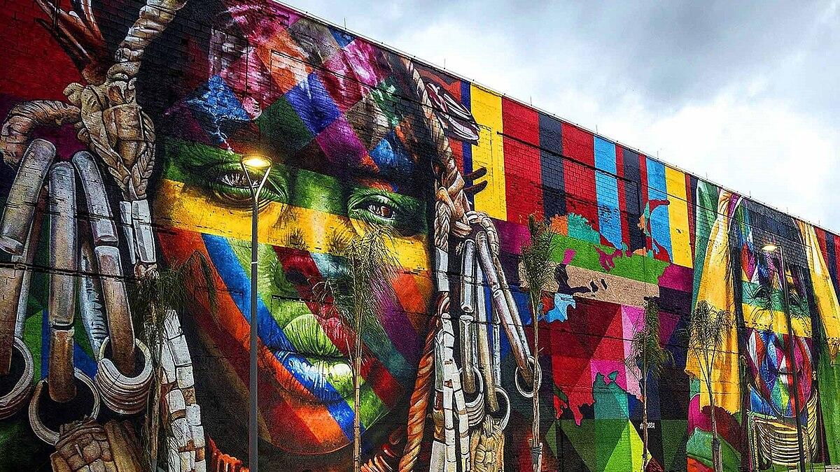 Vibrante mural con un colorido retrato de una persona con rasgos faciales llamativos, detalles intrincados y diseños abstractos al fondo.